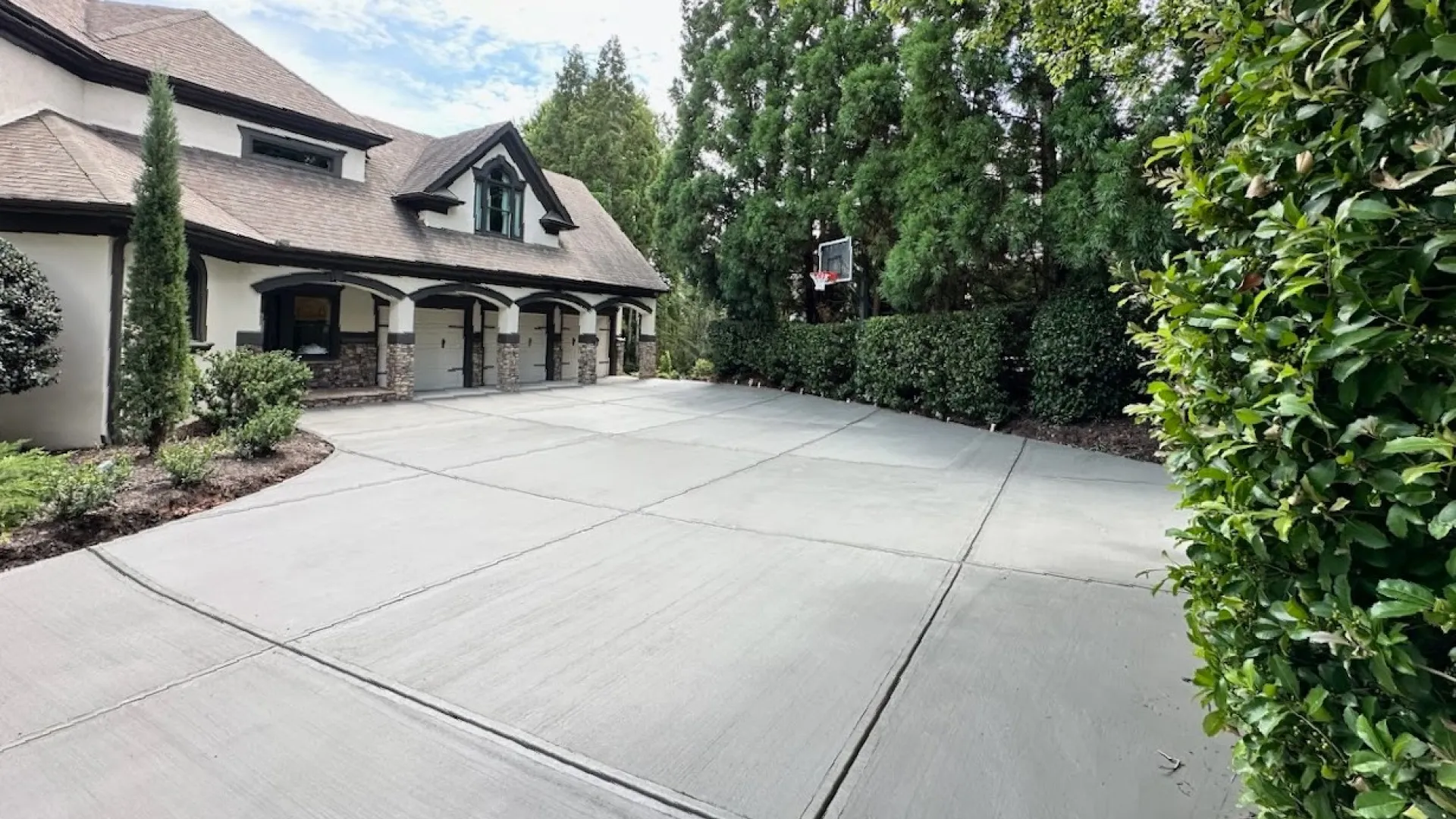 Spacious driveway leading to an elegant home, surrounded by lush greenery and trees under a clear sky.