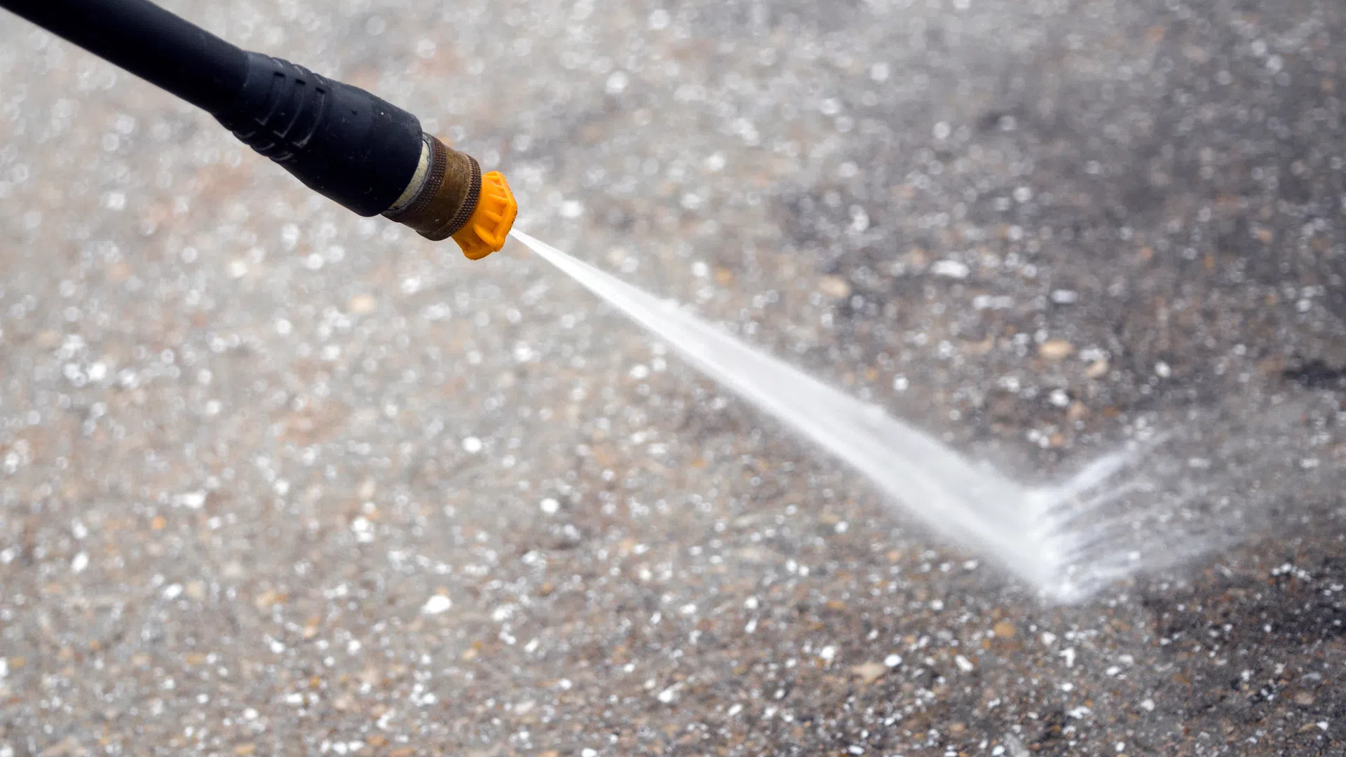 Close-up of a pressure washer nozzle spraying water on a concrete surface, illustrating effective cleaning.