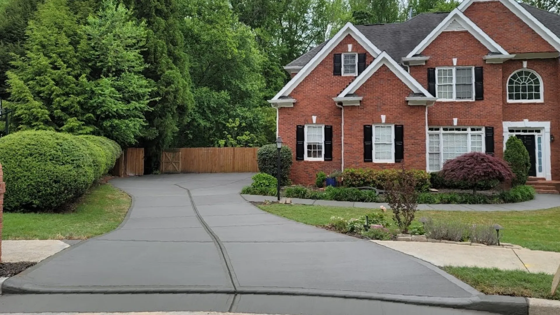 Stylish red brick house surrounded by lush greenery and a neatly paved driveway leading to the entrance.