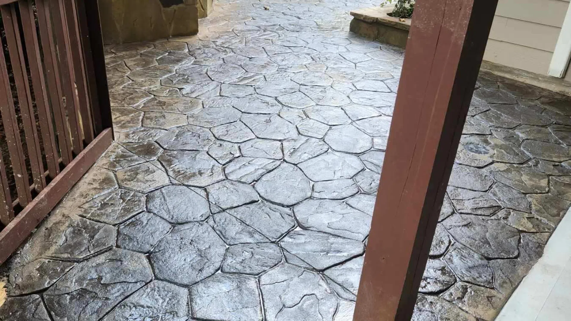 Decorative stamped concrete path with a textured stone pattern, surrounded by greenery and a wooden fence.