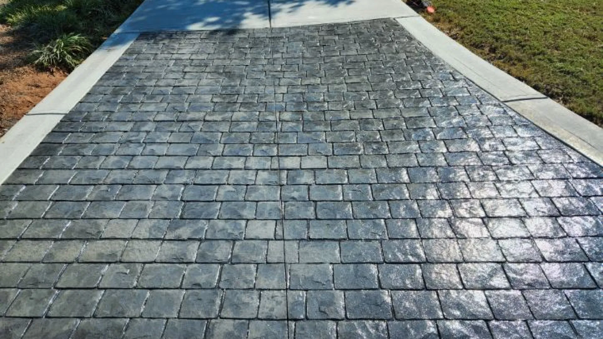 Stamped concrete driveway with a textured stone pattern and smooth concrete border under sunlight.