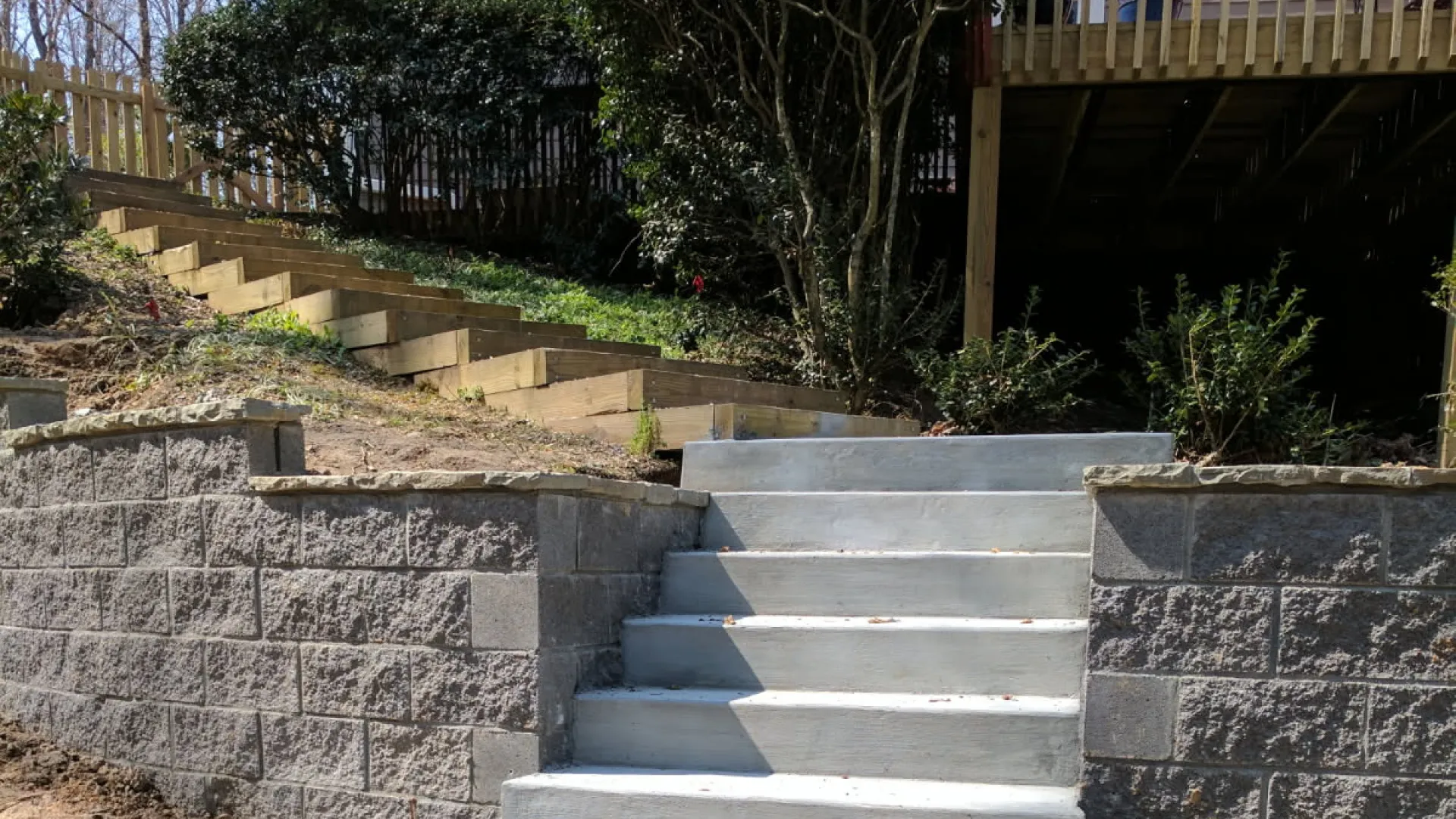 Newly built concrete stairs between retaining walls leading up to a backyard garden and house deck.