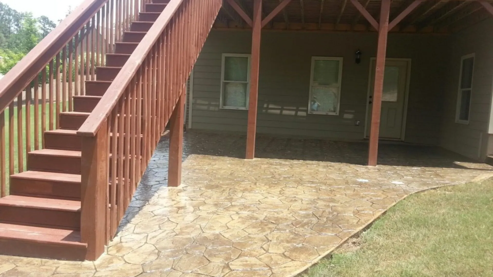 Beautifully designed backyard with stamped concrete patio and wooden stairs leading to a deck.