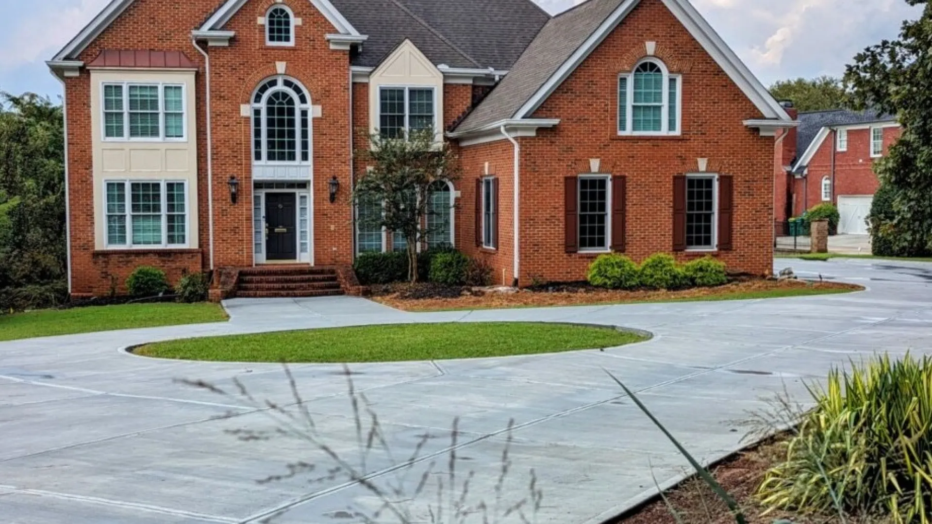 Elegant brick home with large windows and a spacious driveway under a bright sky.