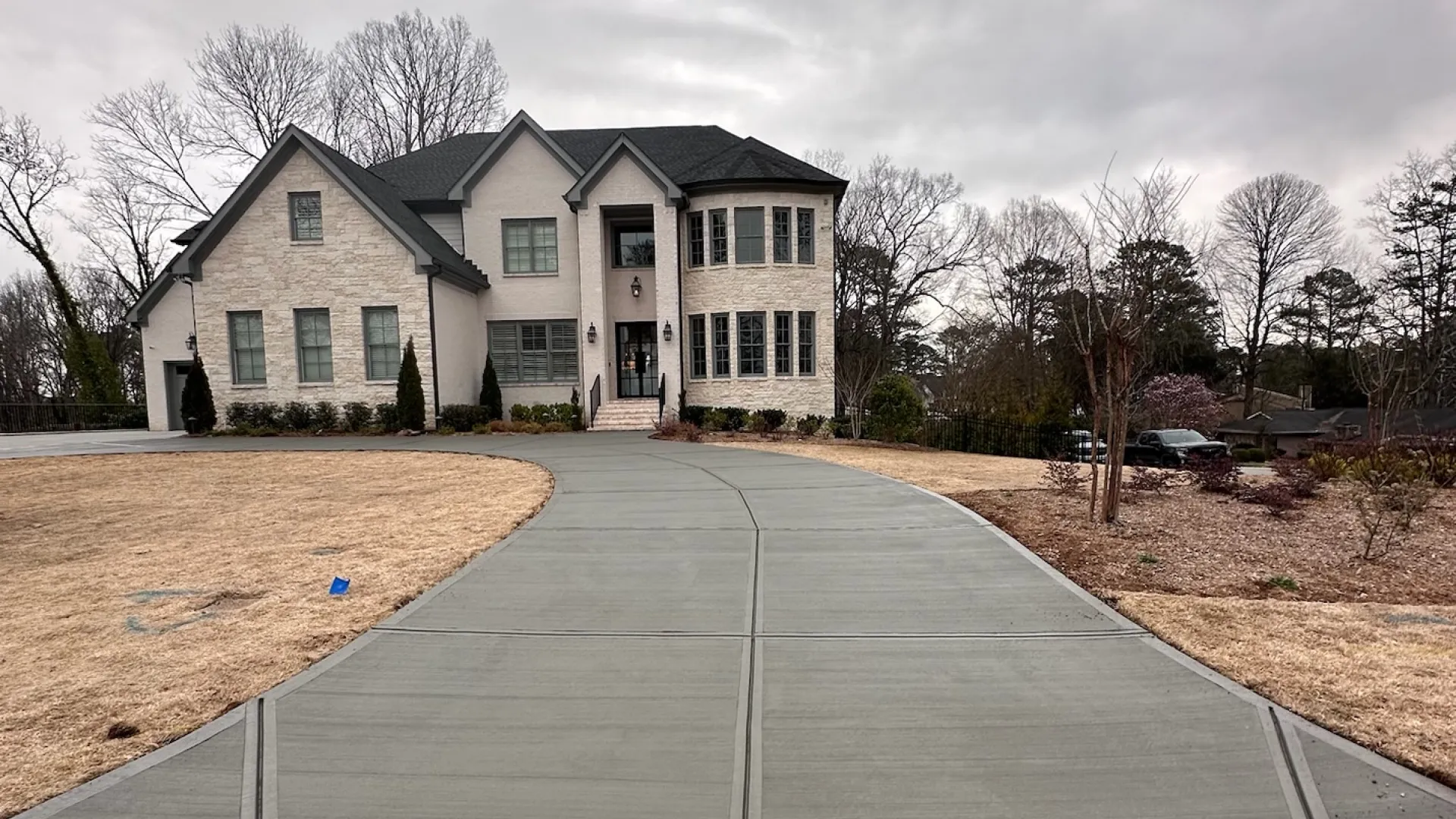 Modern two-story house with a driveway and cloudy sky in the background, showcasing elegant architecture.