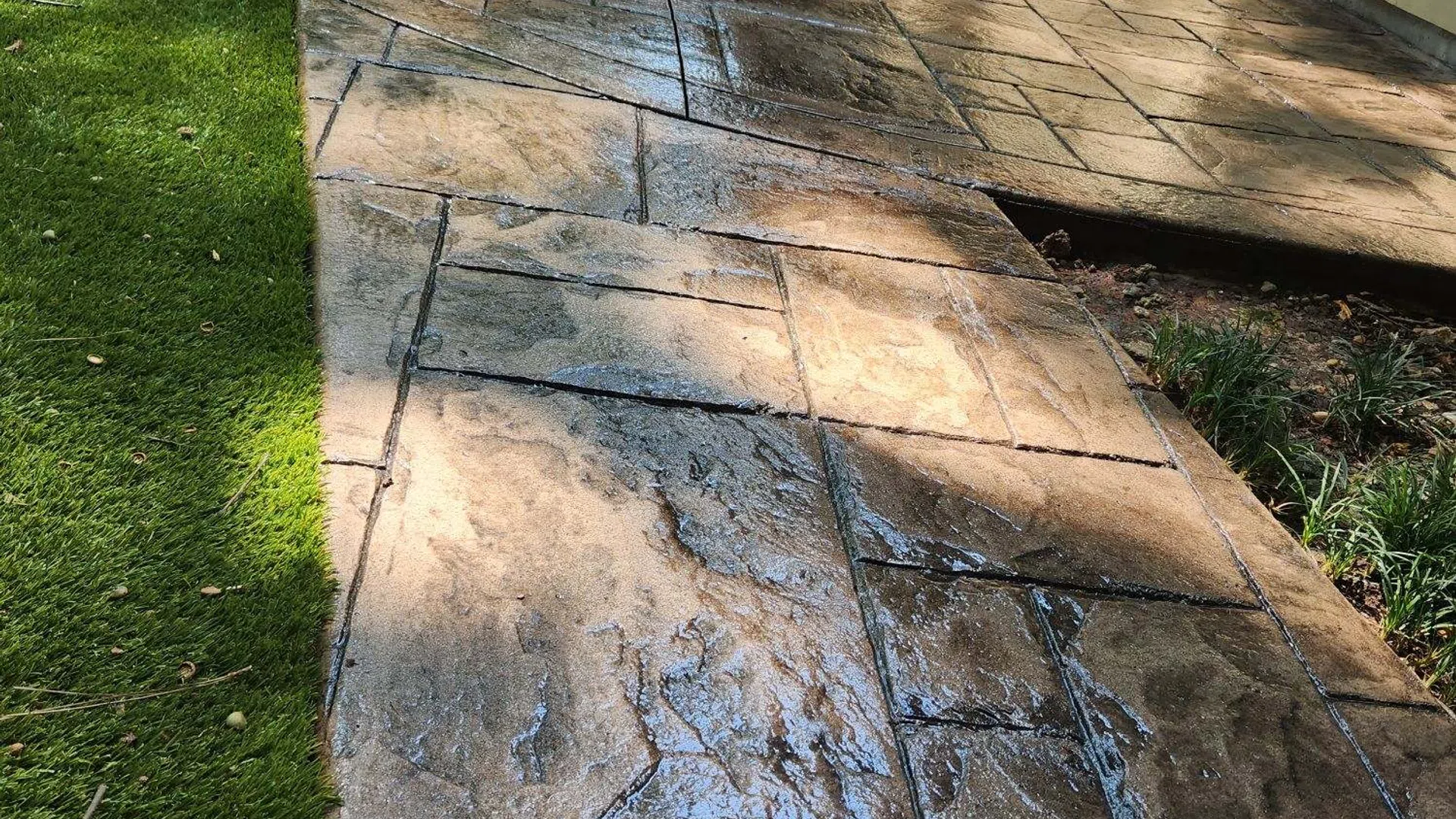 Beautifully stamped concrete pathway with a glossy finish, surrounded by green grass and sunlight.