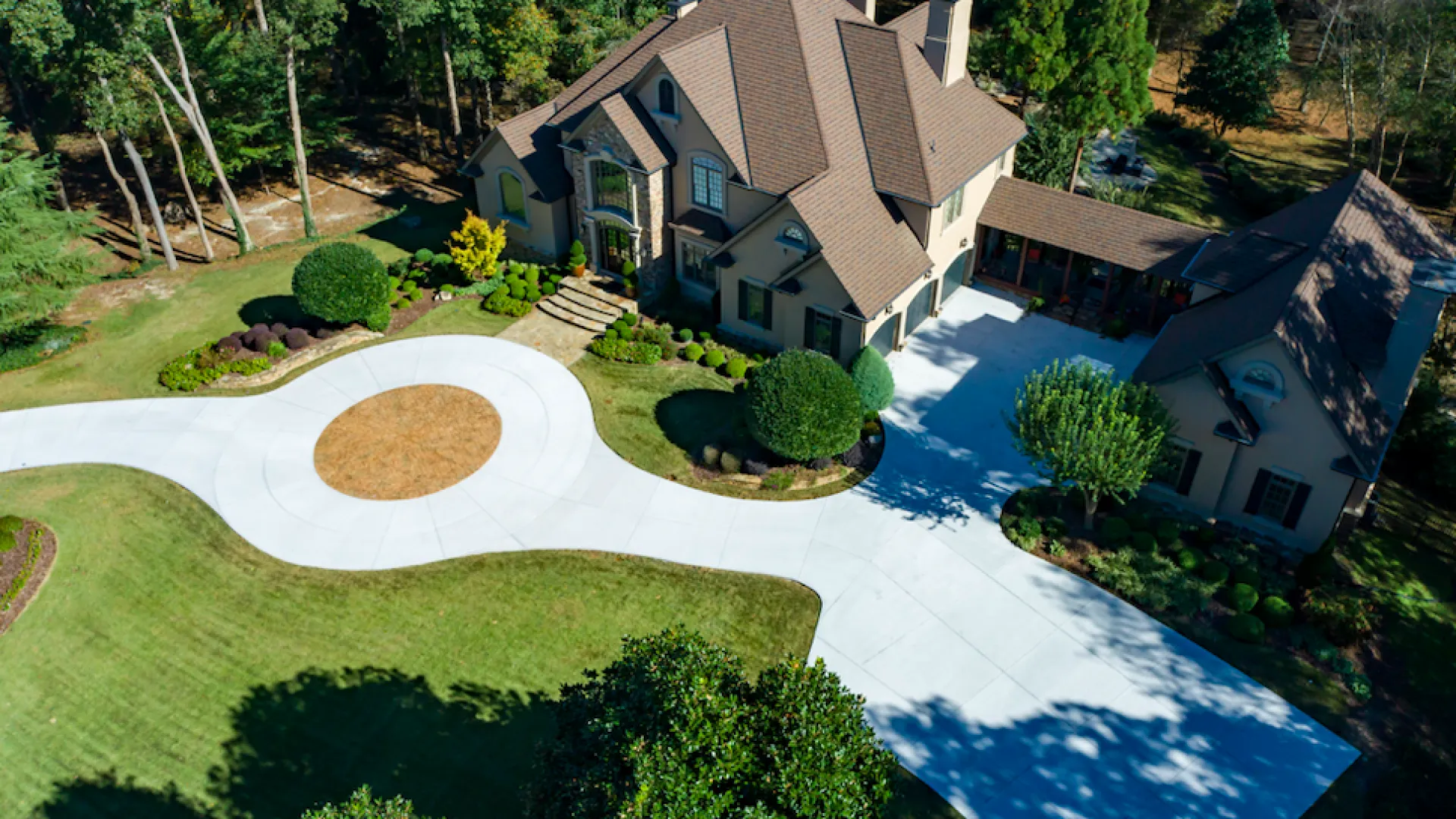 Aerial view of a beautifully landscaped home with a circular driveway and lush greenery surrounding it.