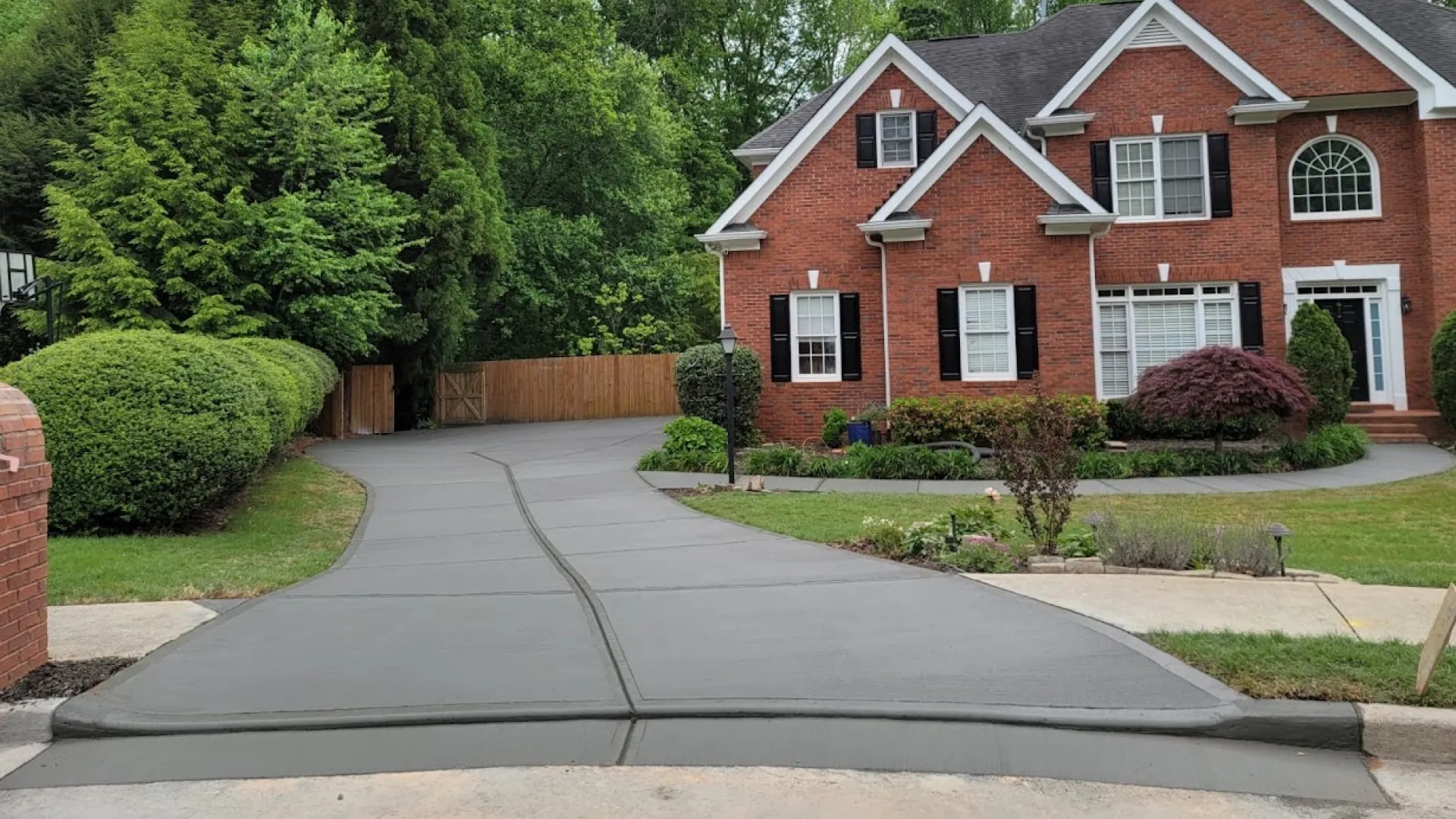Beautiful brick house with a manicured yard and a freshly paved driveway surrounded by greenery.