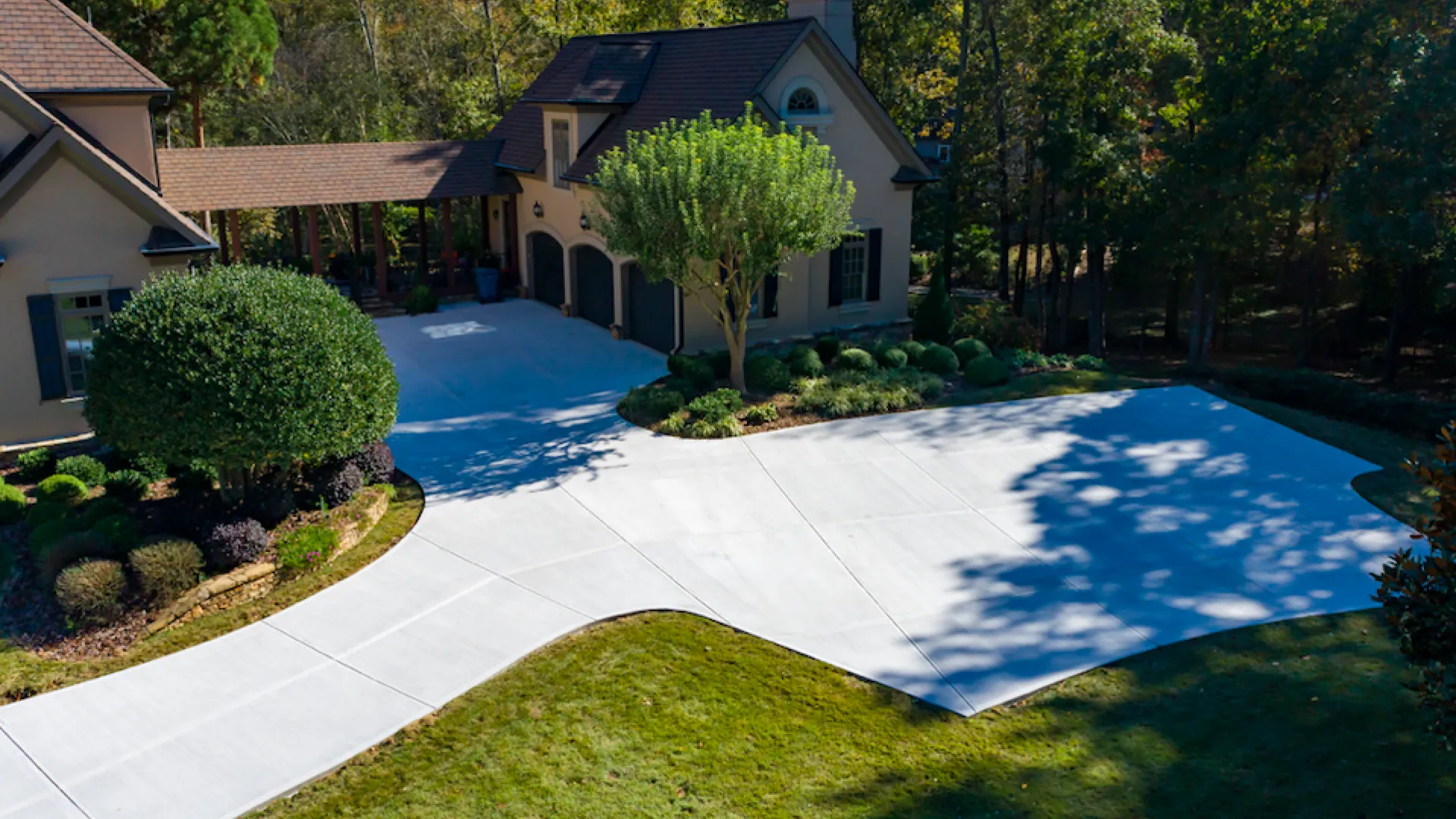 Aerial view of a modern driveway and landscaped yard beside a beautiful house, surrounded by trees.