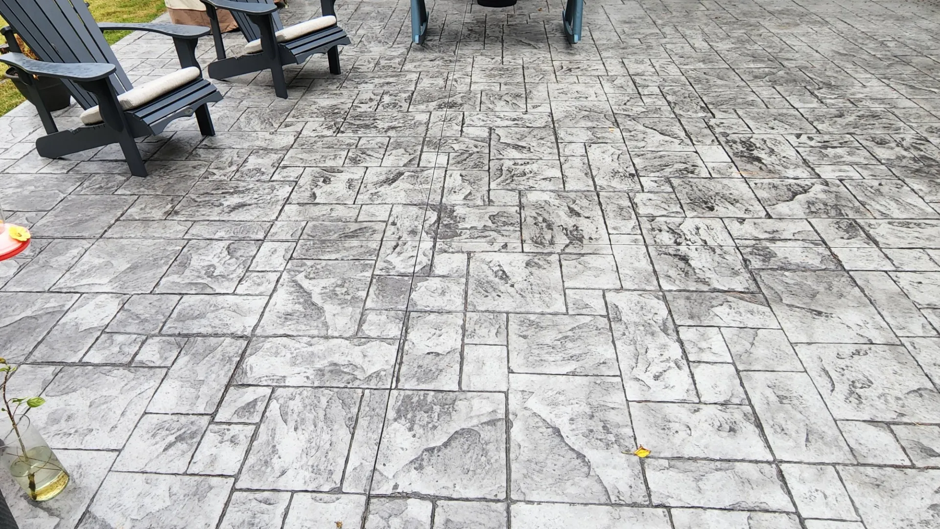 Gray stamped concrete patio with two black adirondack chairs and a cozy outdoor setting.