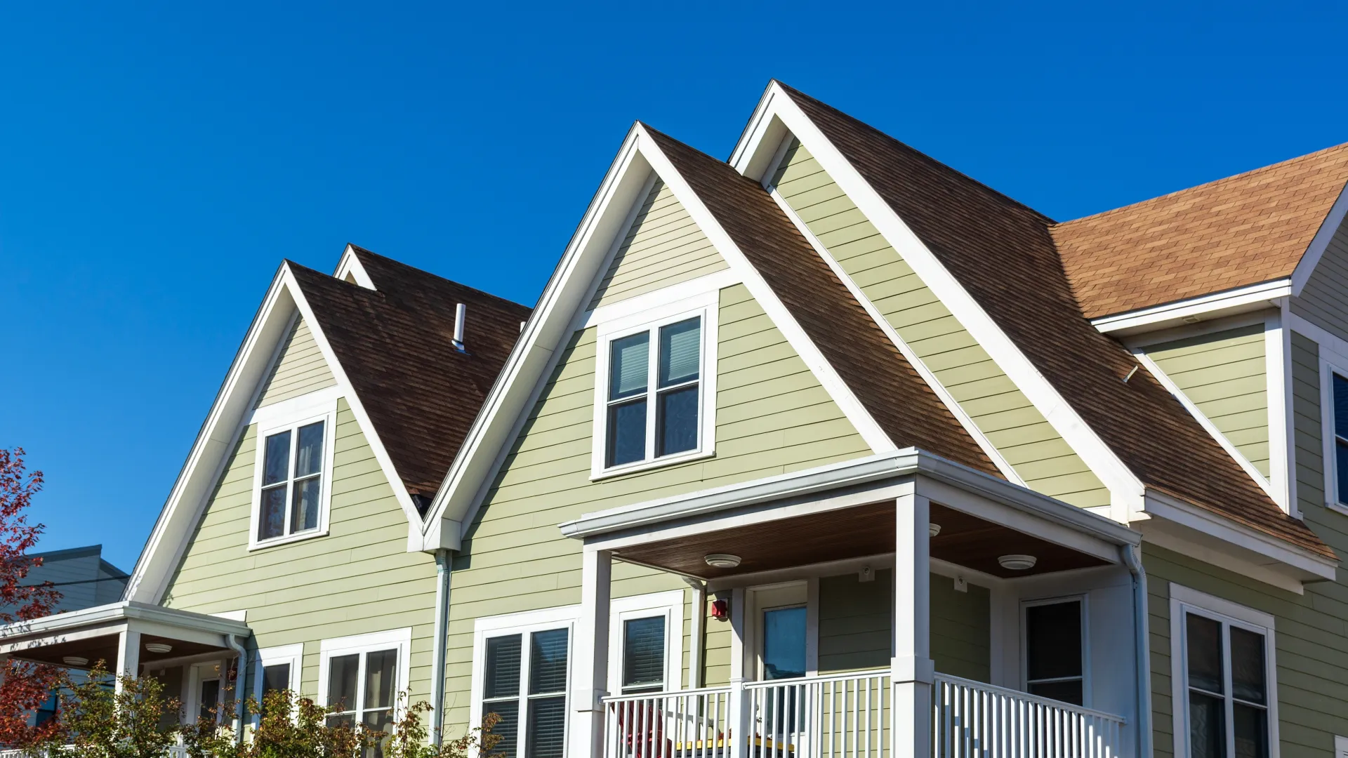 Modern suburban green house with white trim and porch under a clear blue sky