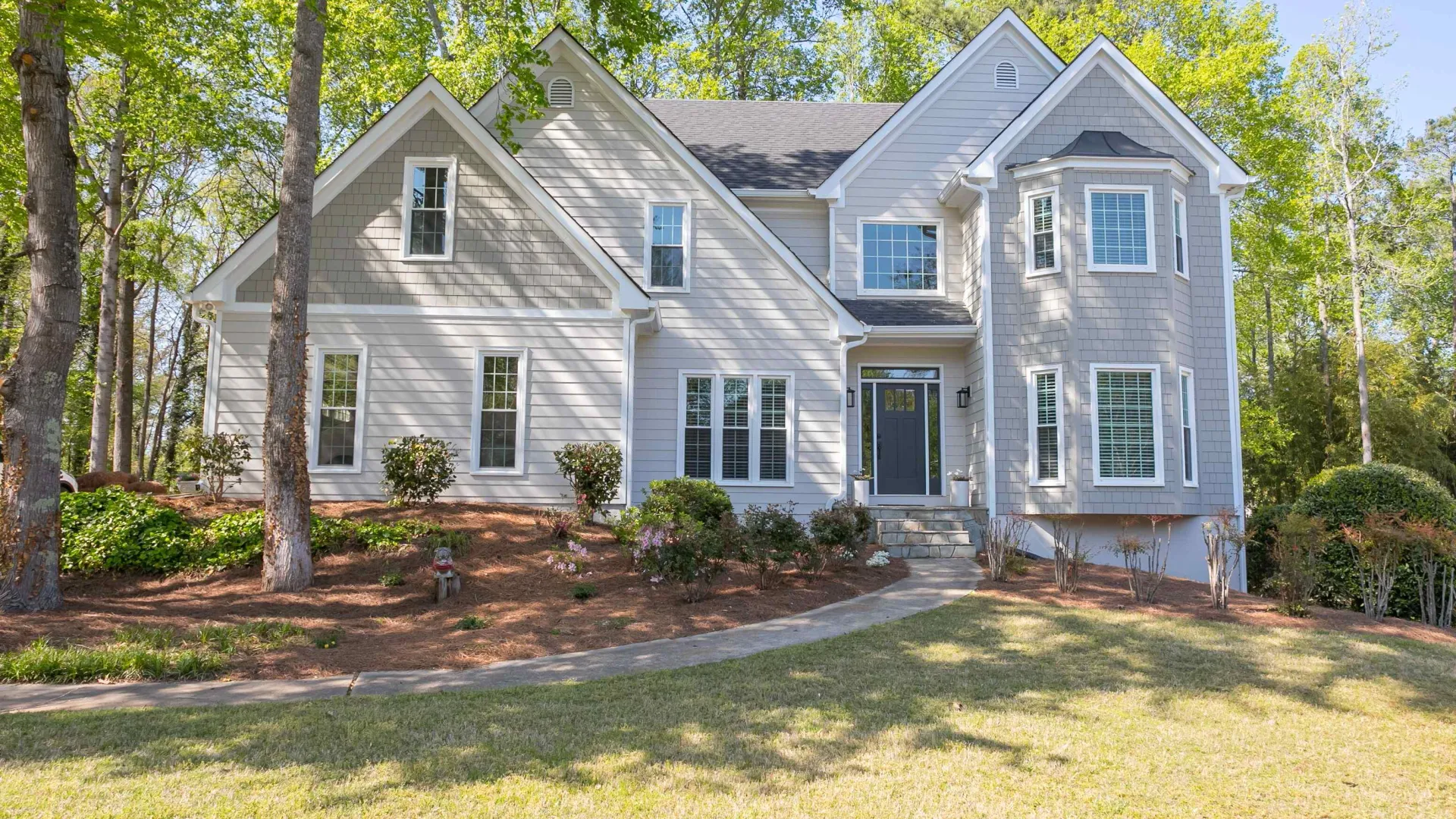 Modern two-story gray house with multiple windows and a manicured lawn surrounded by trees on a sunny day