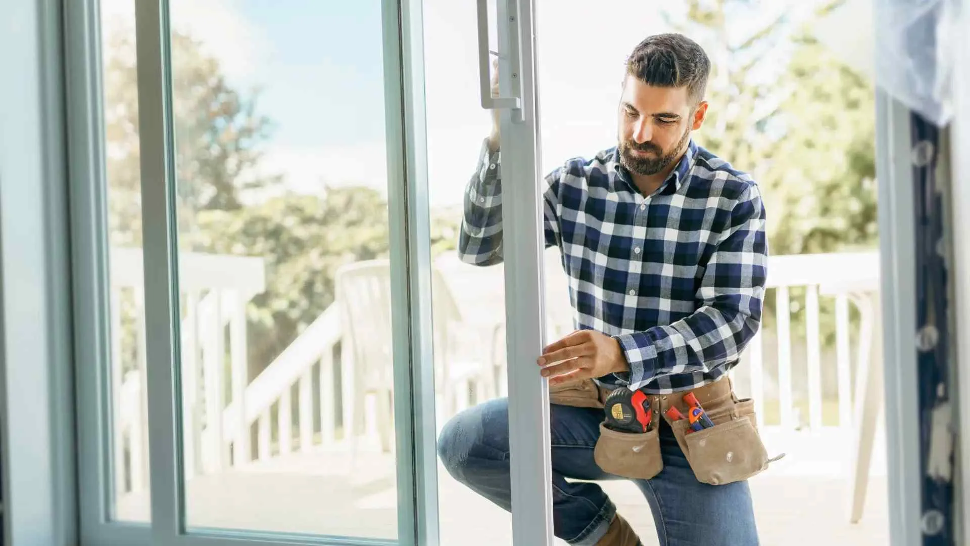 Man with tool belt installing or repairing sliding glass door in bright home setting.