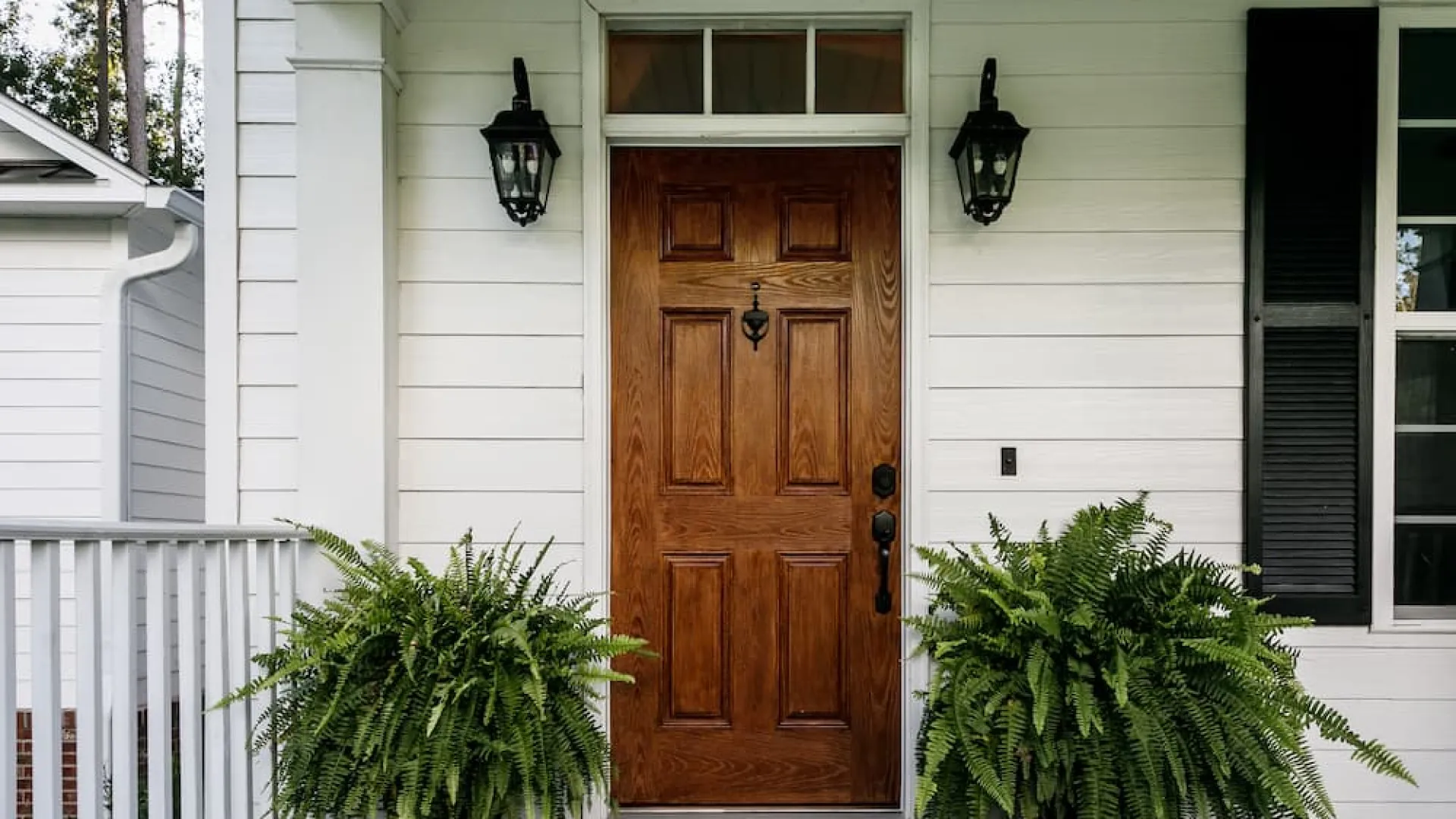 Traditional wood grain entry door with decorative hardware and exterior porch lighting, emphasizing front door repair.
