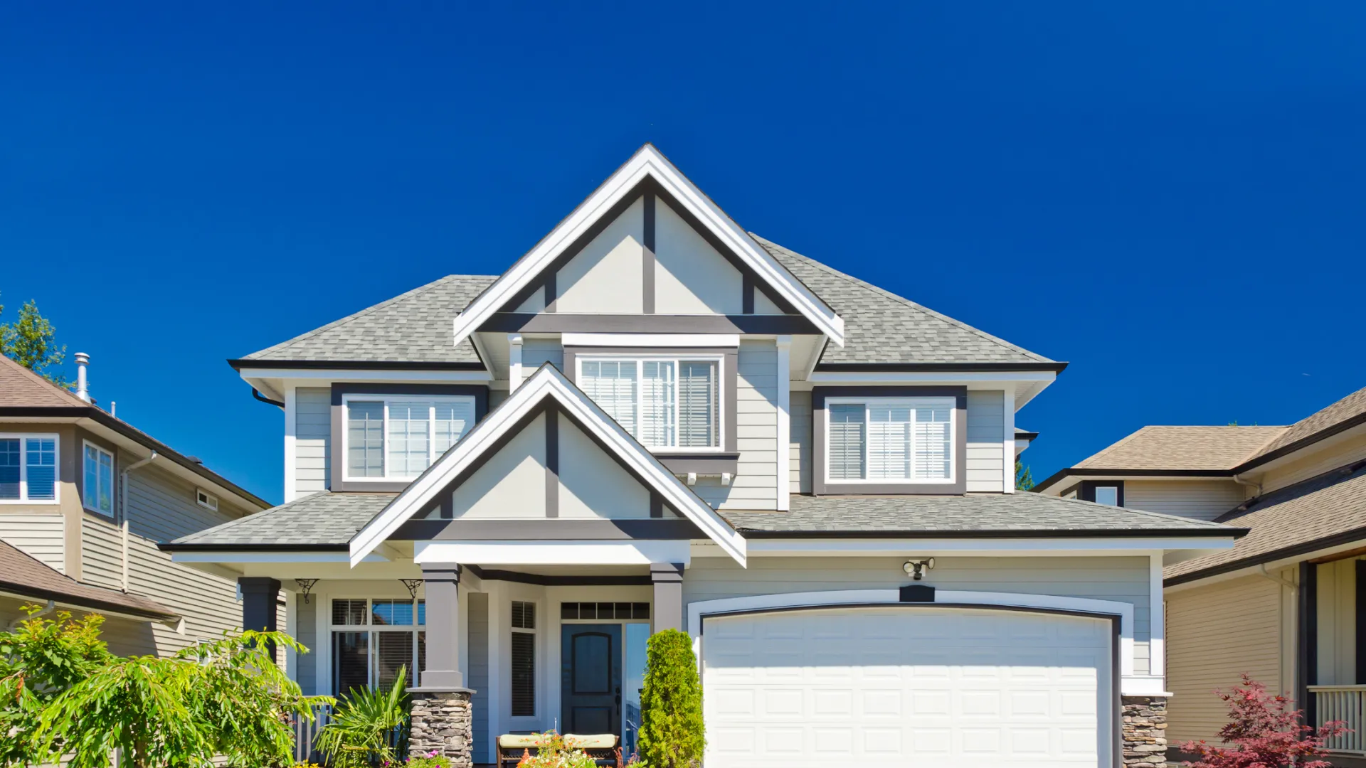 Modern two-story house with gray siding, white trim, landscaped front yard, and clear blue sky background