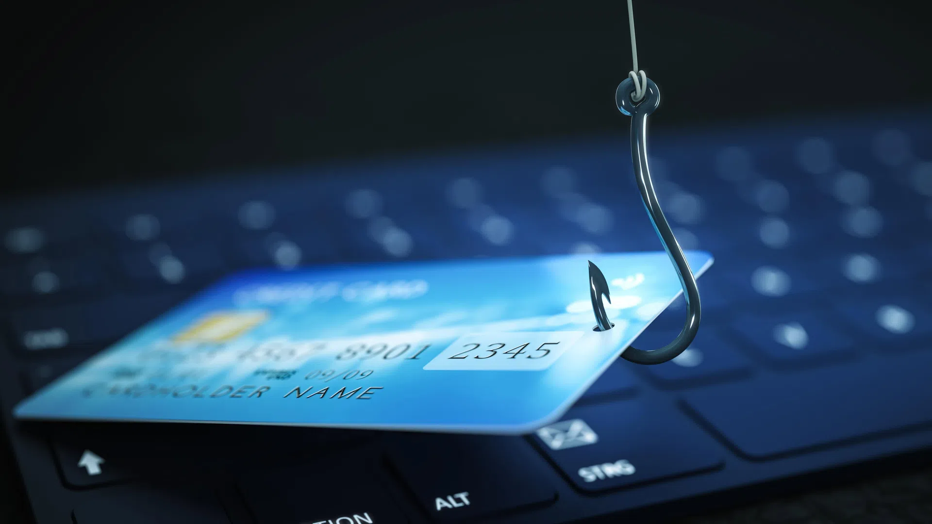 Credit card pierced by a fishing hook on a keyboard symbolizing online fraud and phishing scams.