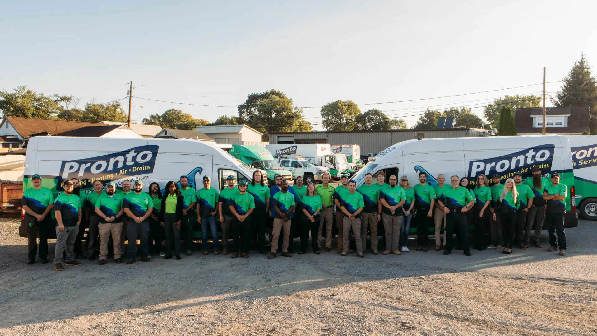 Large team of uniformed Pronto HVAC technicians standing in front of branded service vans in a sunny outdoor lot.