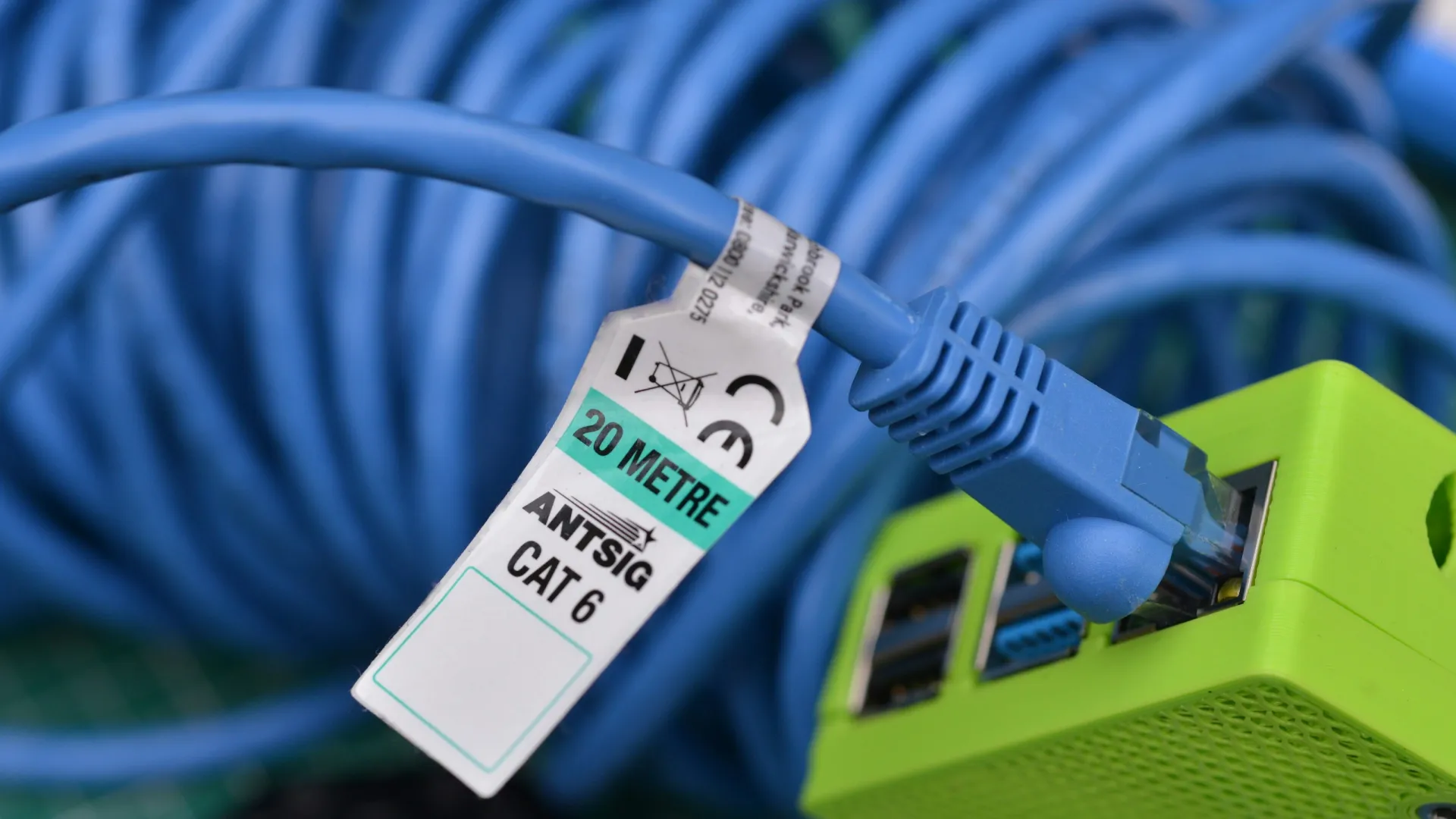 Close-up of a blue CAT 6 Ethernet cable with a 20 metre label plugged into a green network device.
