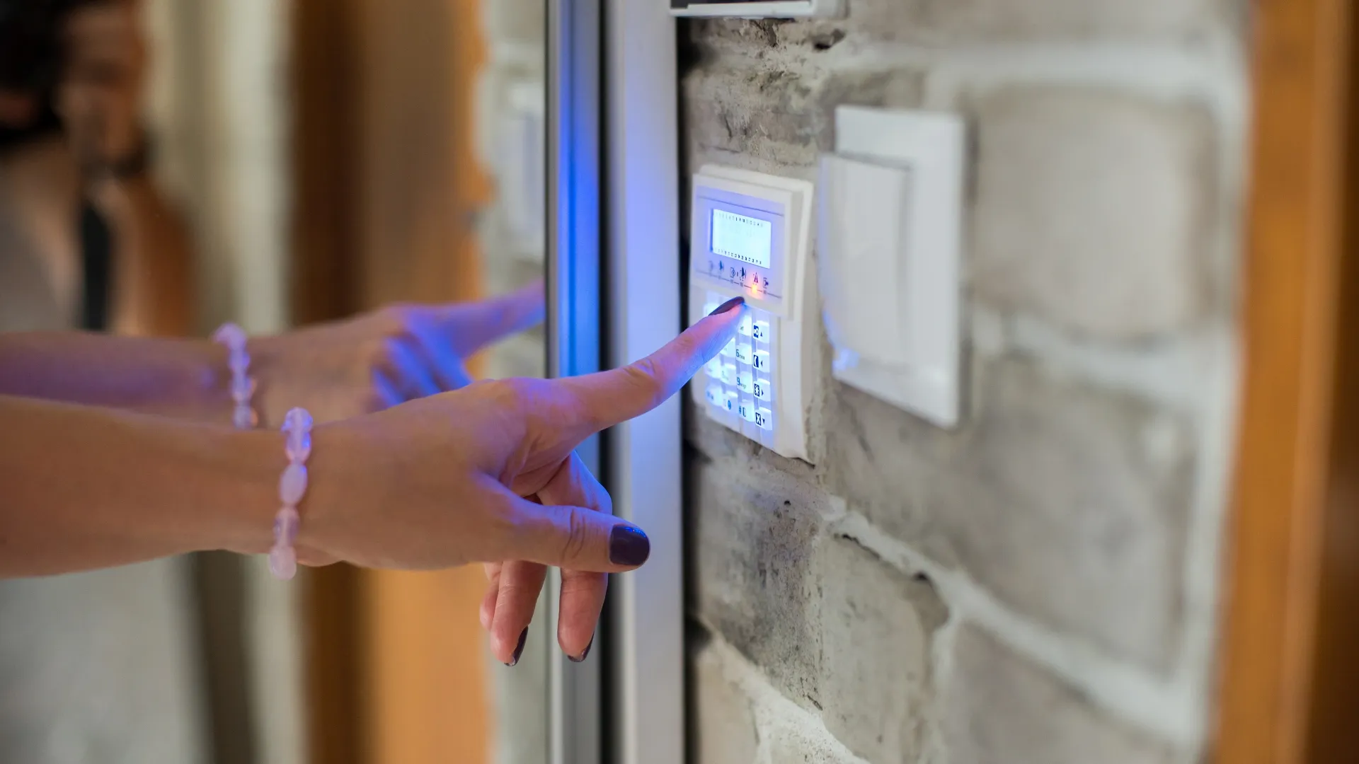 Person using a keypad security alarm system mounted on a stone wall near a door.