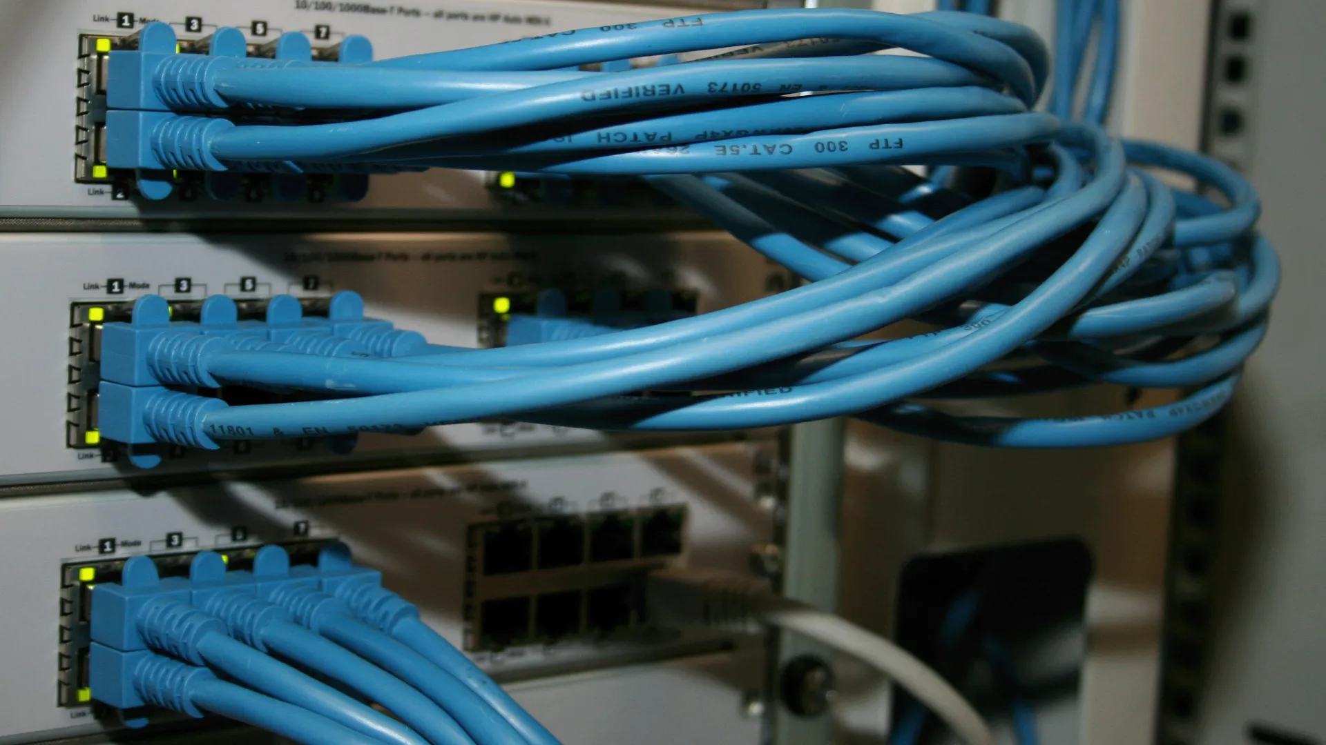 Blue Ethernet cables connected to network switches with active LED status lights in a server rack.