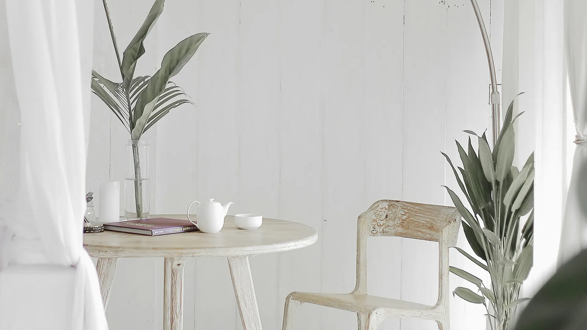 a white table with a white chair and a white table with a white wall with a plant and