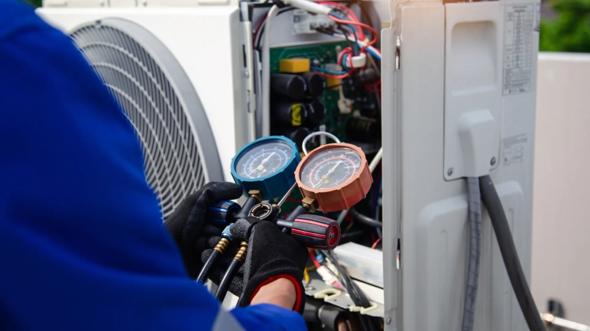 Technician using gauges to service an air conditioning unit outdoors.