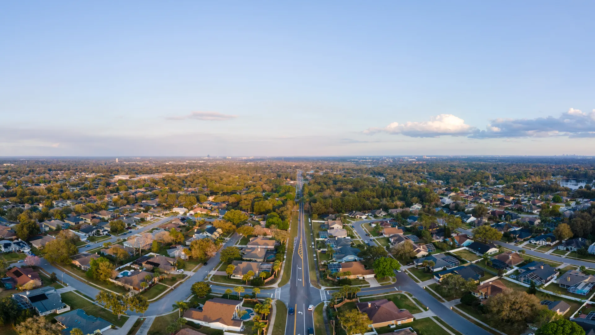 Aerial view of suburban neighborhood with streets, houses, and green trees under a clear sky.