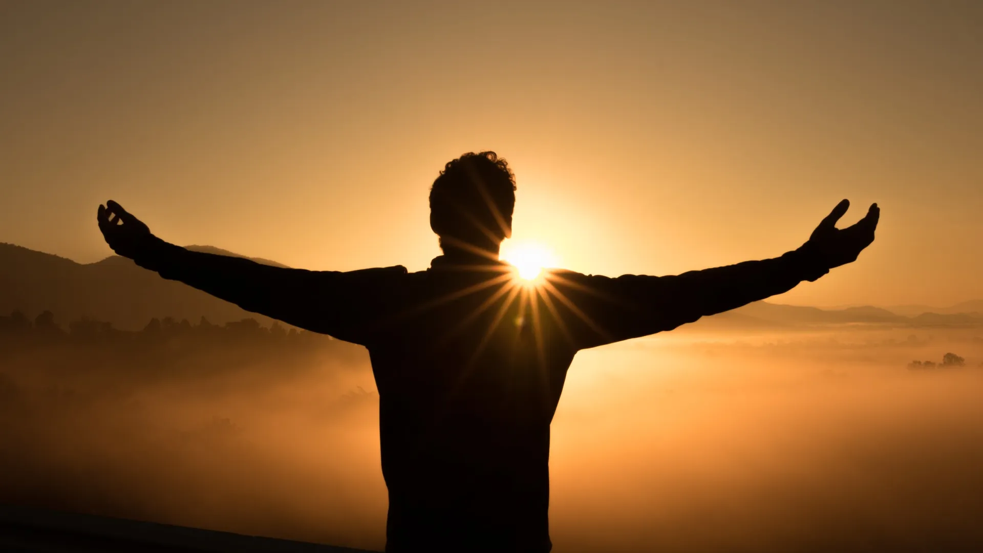 a person with the arms raised in front of the sun