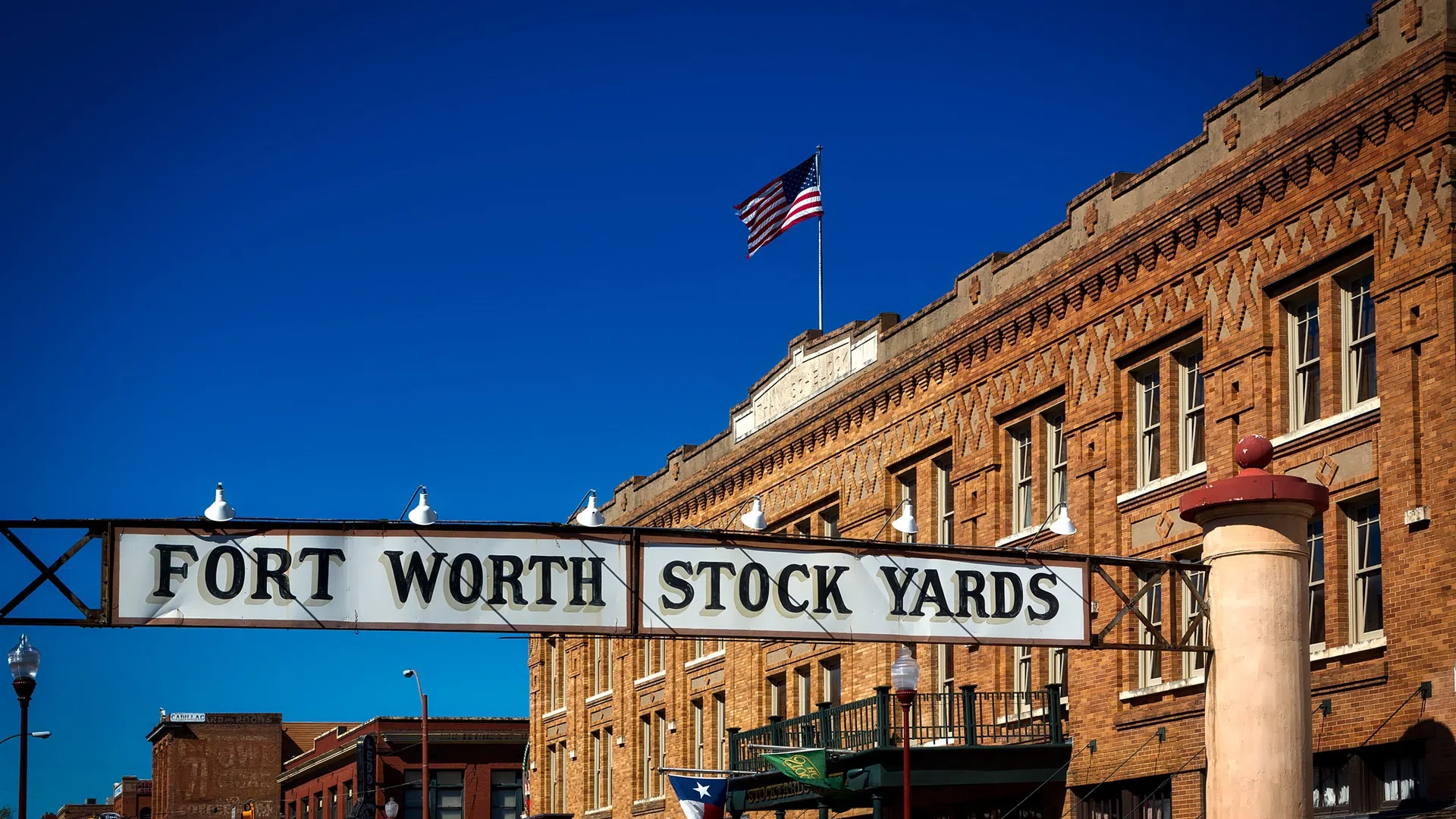 Entrance sign for Fort Worth Stock Yards with historic brick buildings under a clear blue sky.