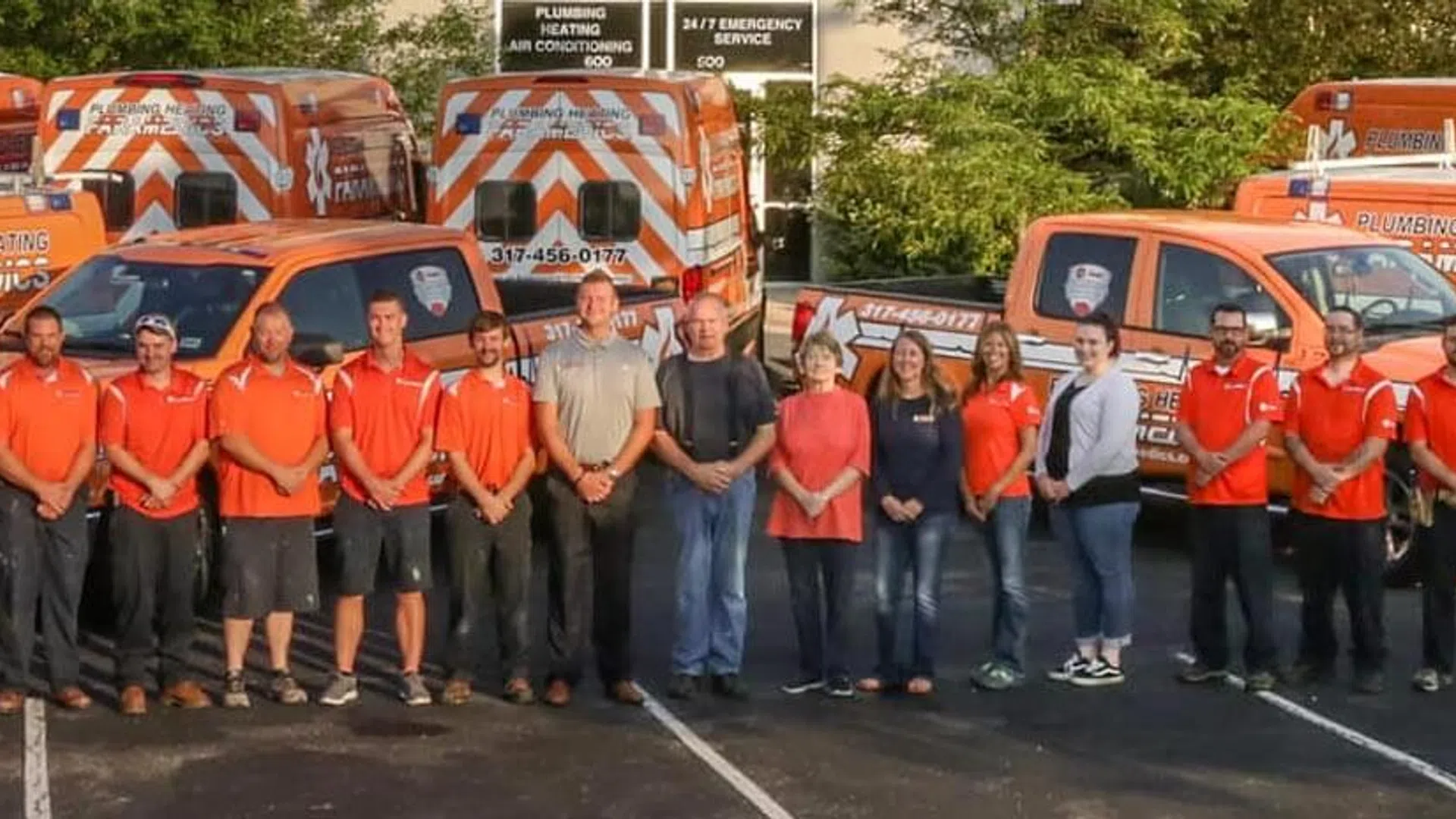 Paramedics and staff standing in front of a fleet of orange emergency response vehicles in a parking lot.