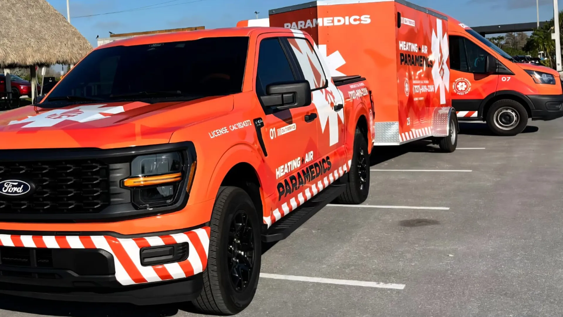 Orange paramedics truck, trailer, and van parked in a lot under blue sky with visible medical crosses.