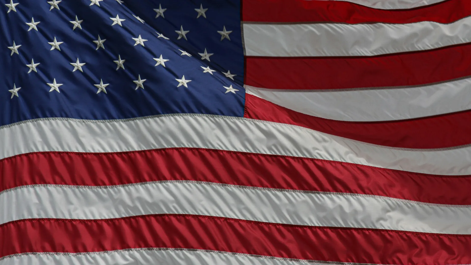 Waving American flag with red and white stripes and white stars on blue field in close-up view