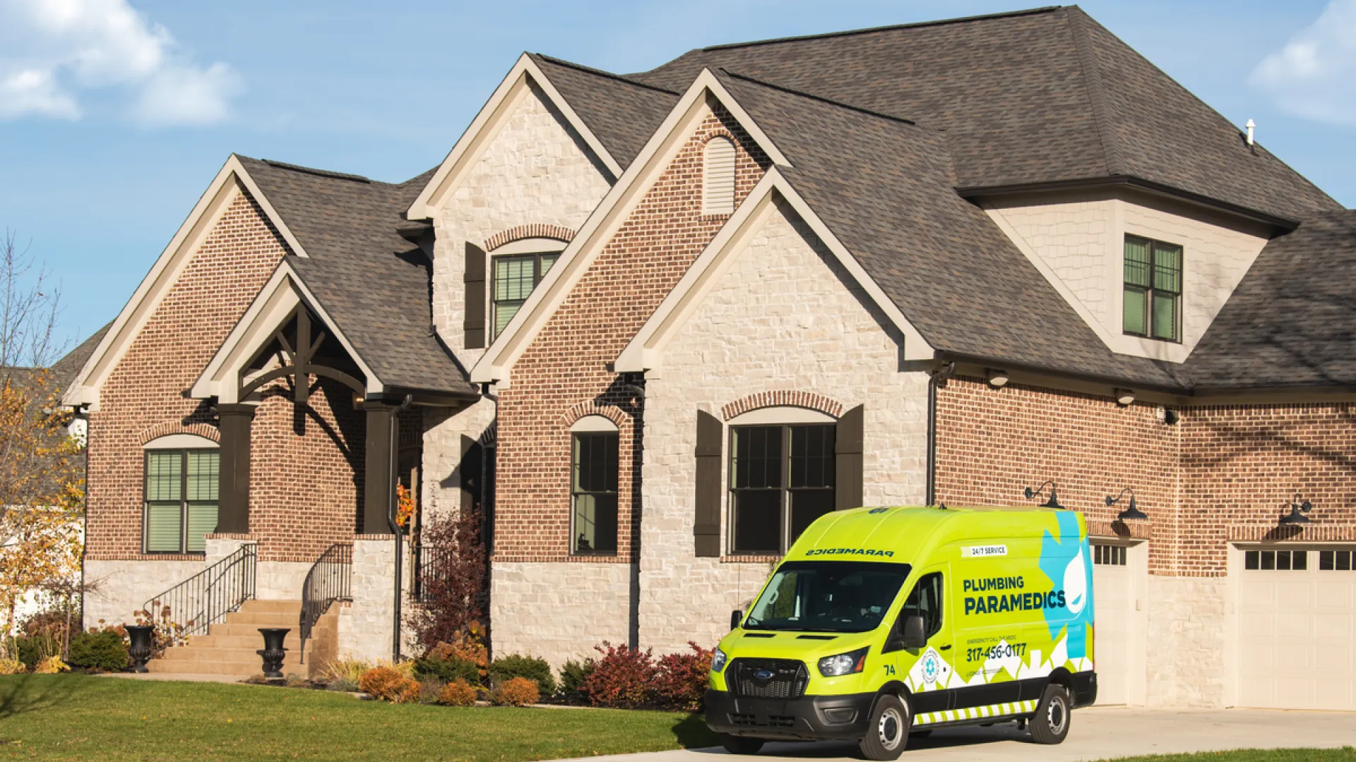 A colorful Plumbing Paramedics van parked in front of a large, elegant brick house.