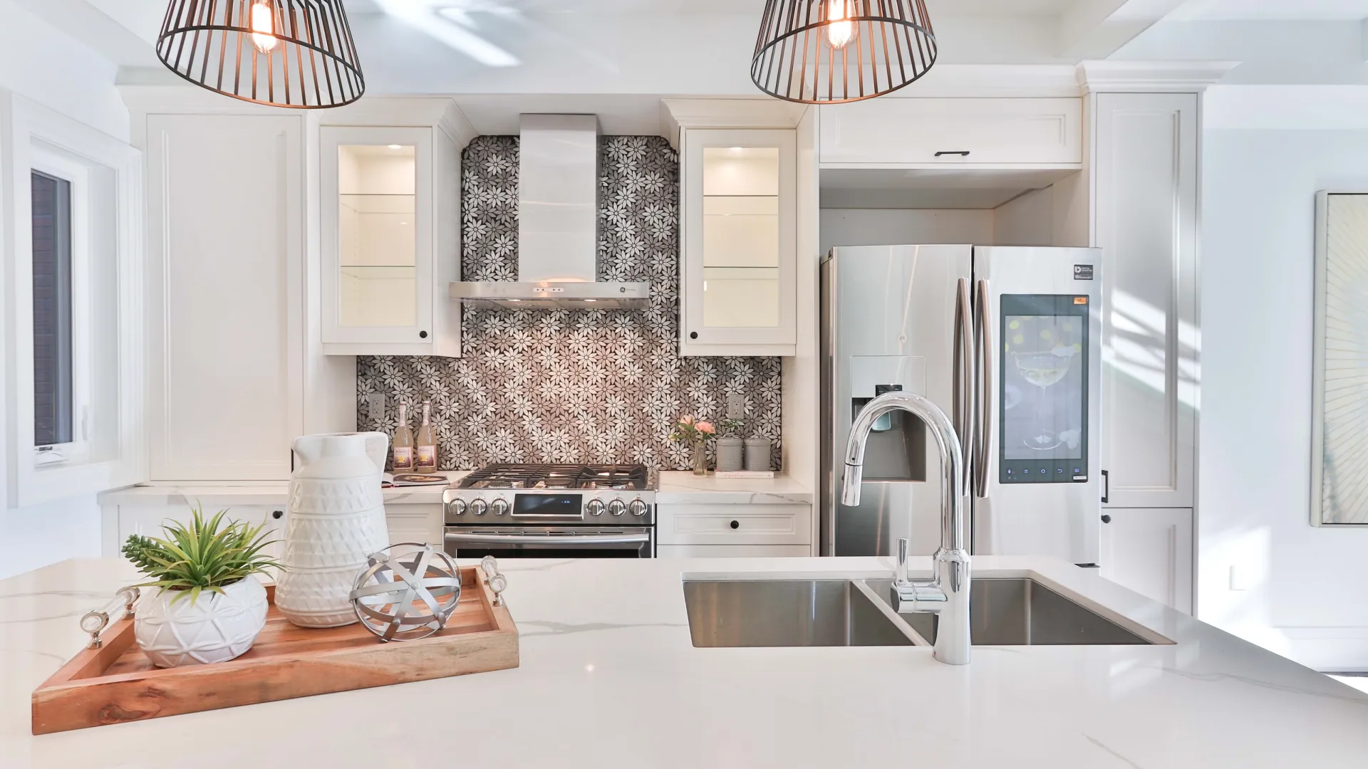 Modern white kitchen with marble countertops, stainless steel appliances, pendant lights, and patterned backsplash.