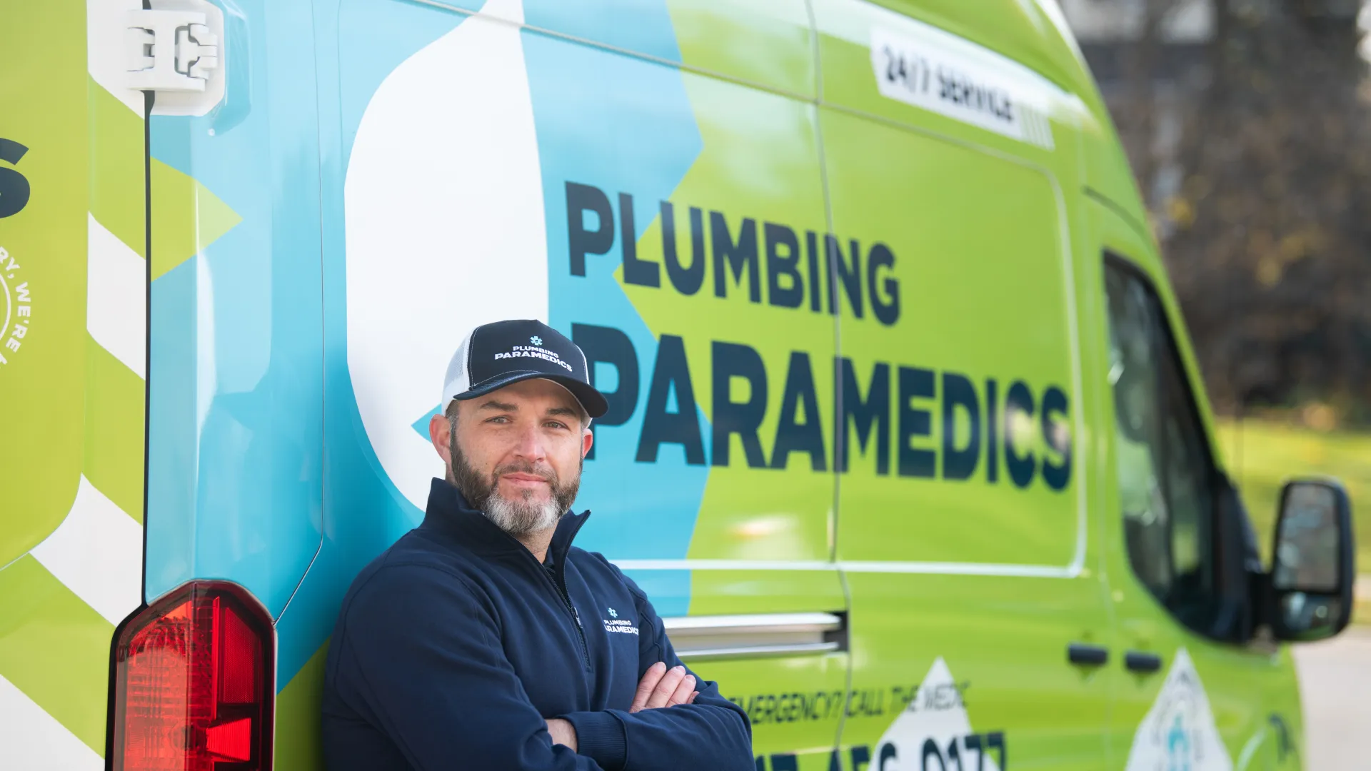 Plumbing paramedics technician standing with arms crossed next to a branded service van outdoors