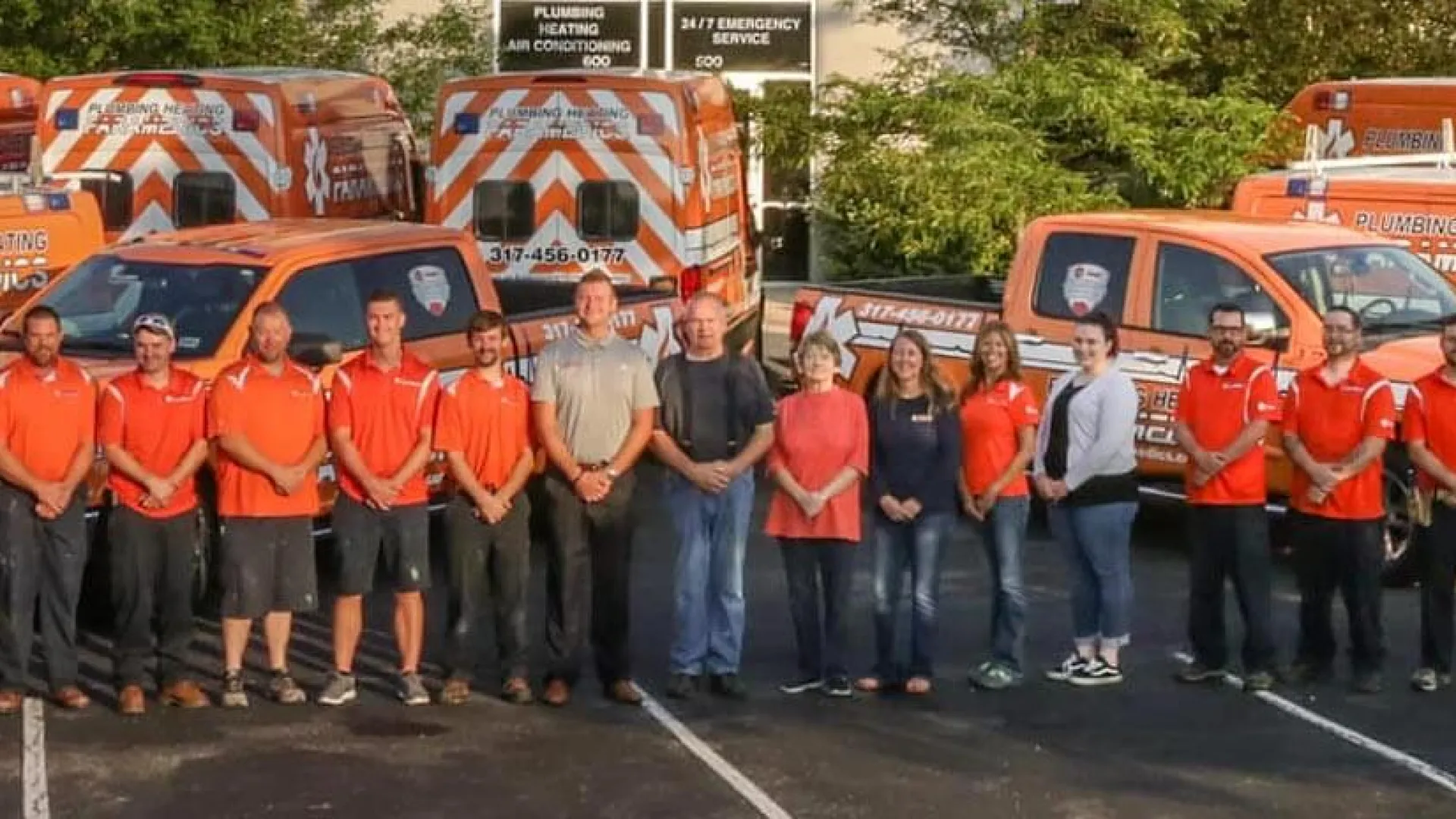 Emergency medical team in orange uniforms standing in front of multiple orange ambulances in a parking lot.