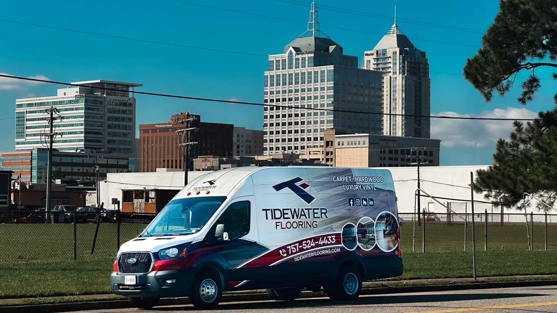 Tidewater Flooring service van parked on city street with high-rise buildings in background on sunny day.