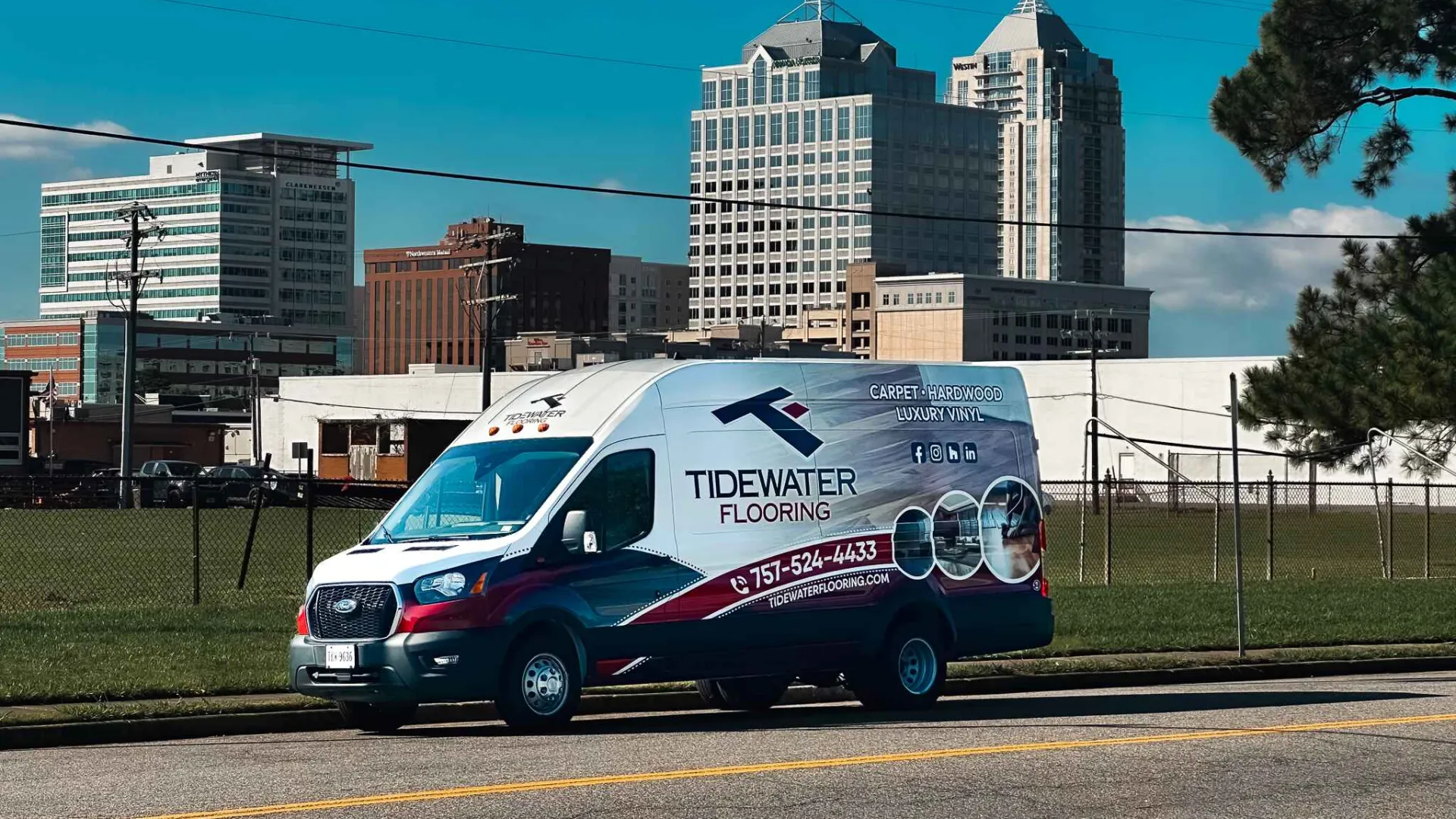 Tidewater Flooring service van parked on city street with high-rise buildings in background on sunny day.