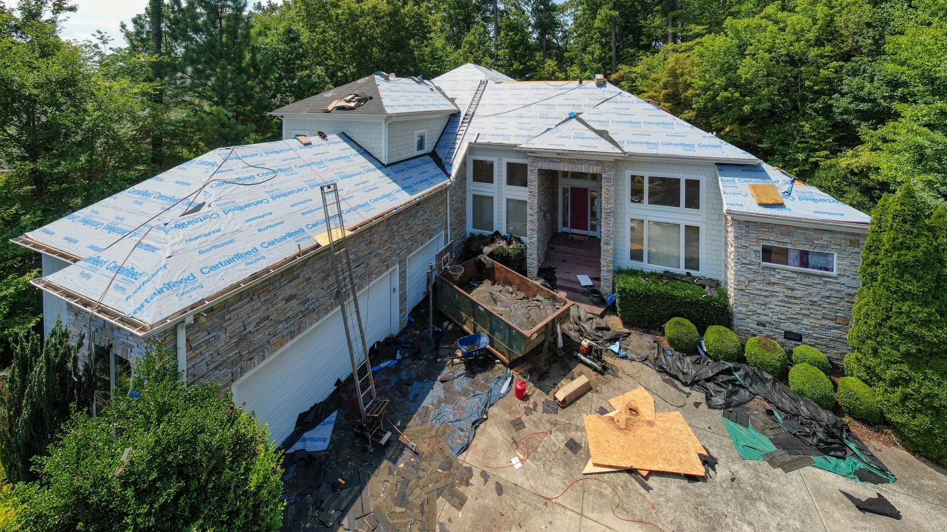 A large house undergoing roof replacement with materials and tools scattered around the driveway.