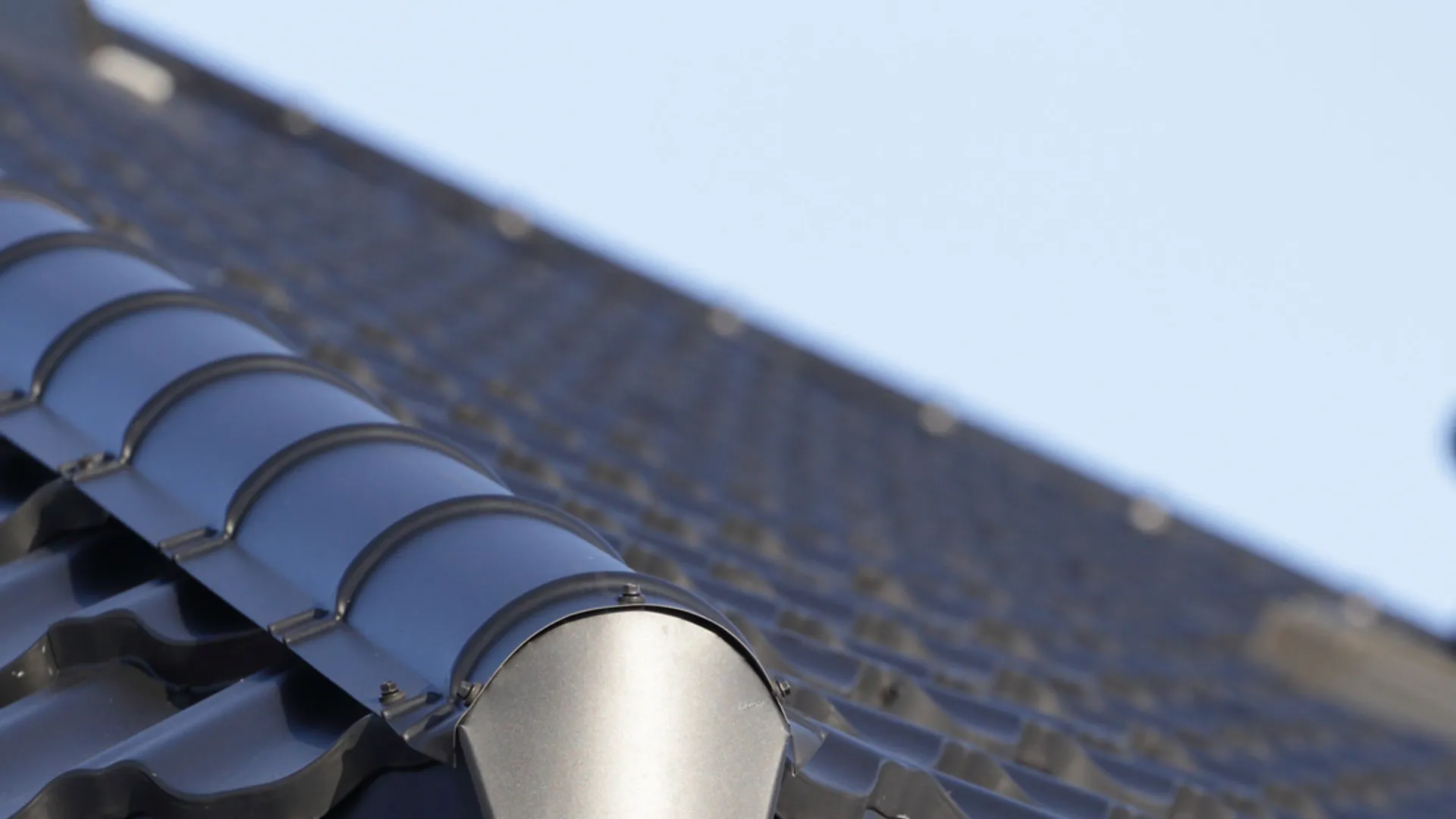 Close-up of black ceramic roof tiles with a clear blue sky background and ventilation pipes.