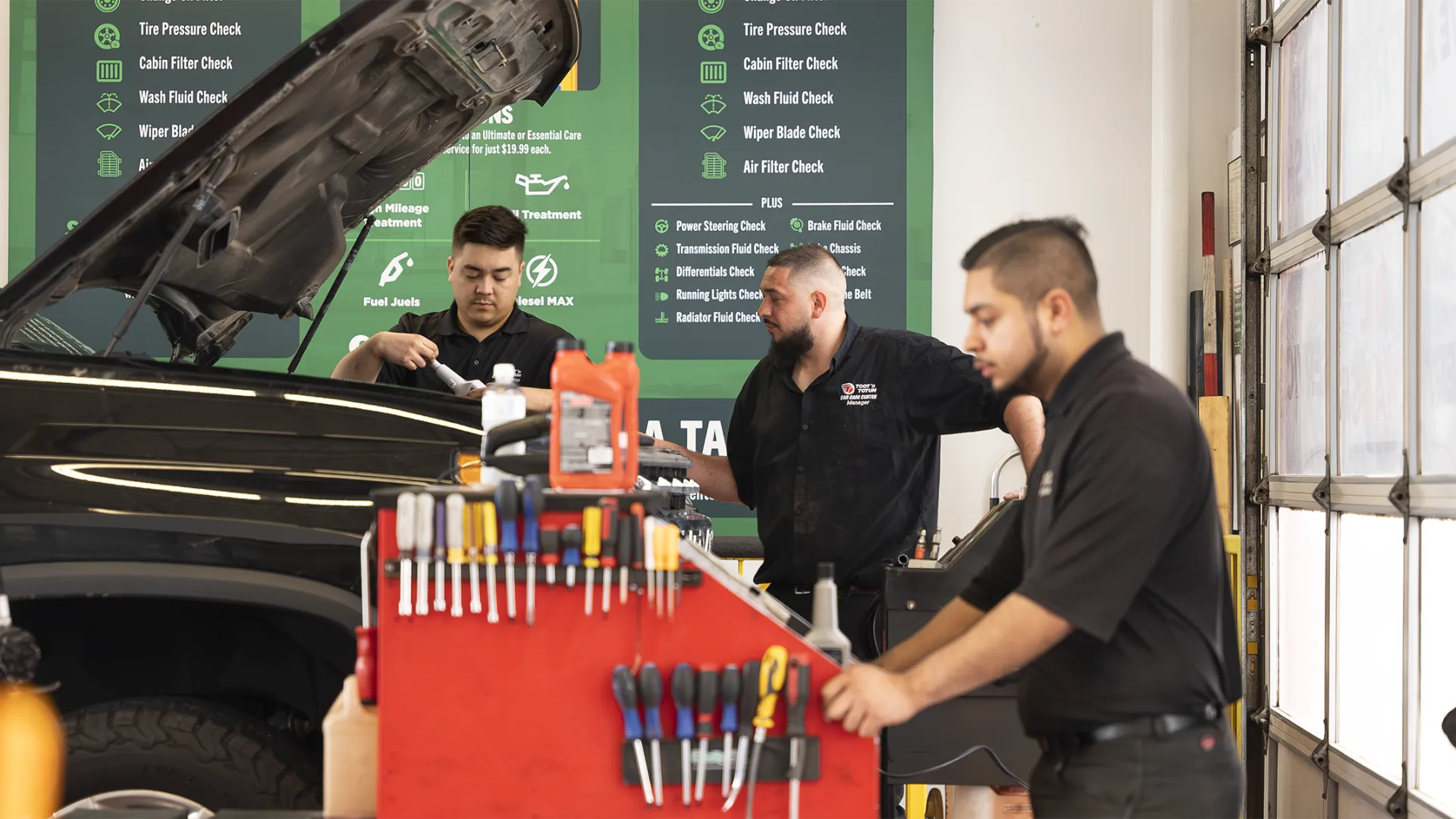 Auto mechanics working on a car in a garage with tools and maintenance checklists visible