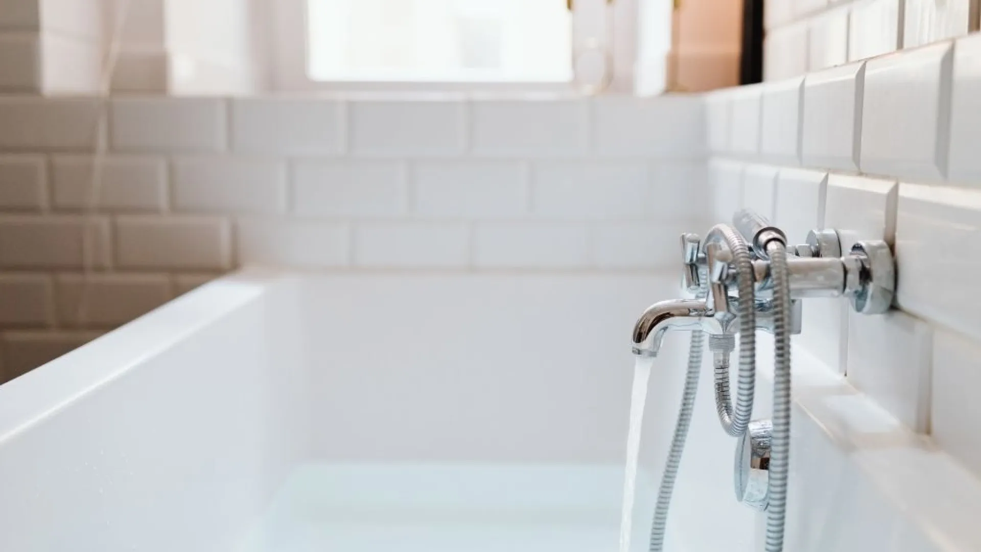 Modern black kitchen faucet with running water over a black sink with blurred kitchen background and vase