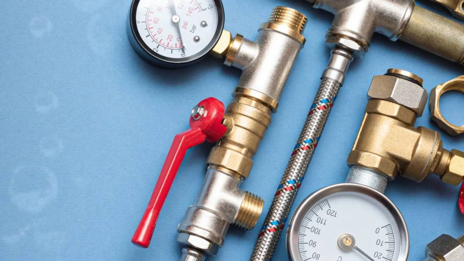 Assorted plumbing tools including pressure gauges, valves, pipes, and connectors on a blue background.