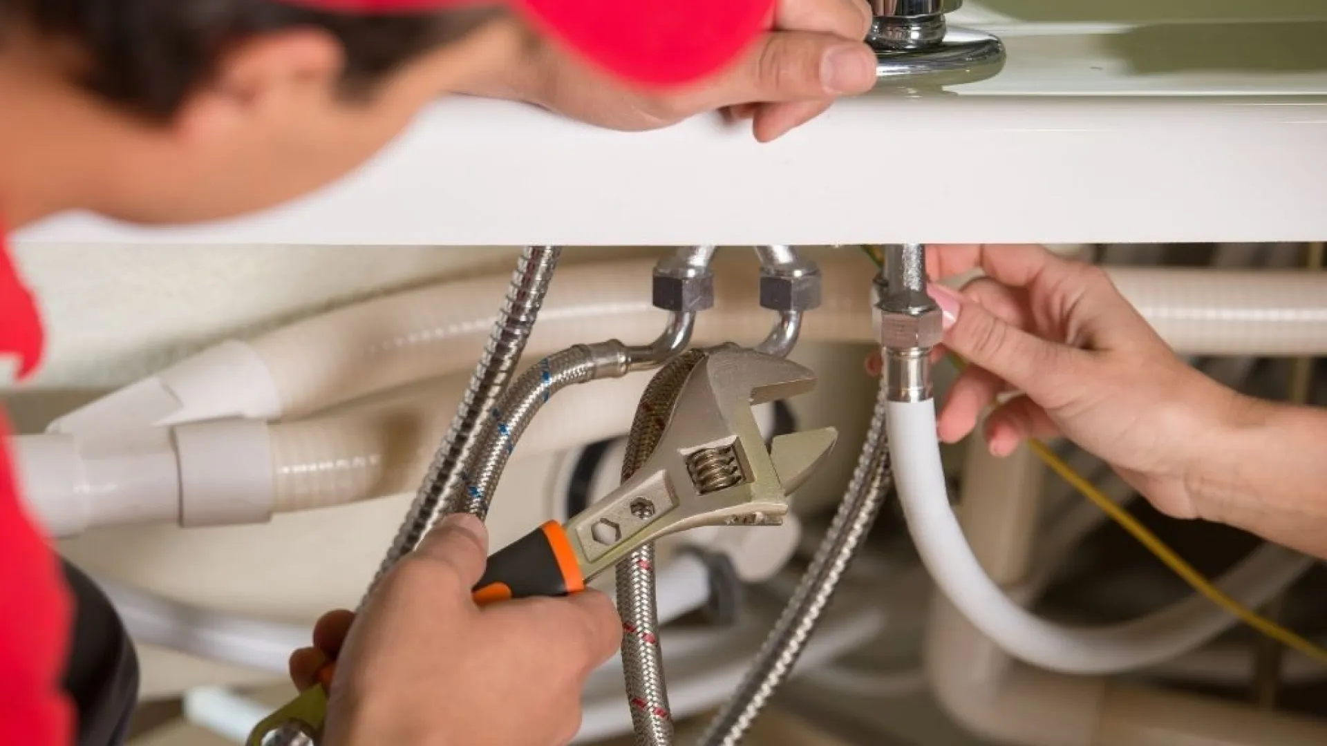 Plumber in blue overalls using a manual drain auger to unclog a white bathroom sink drain effectively.
