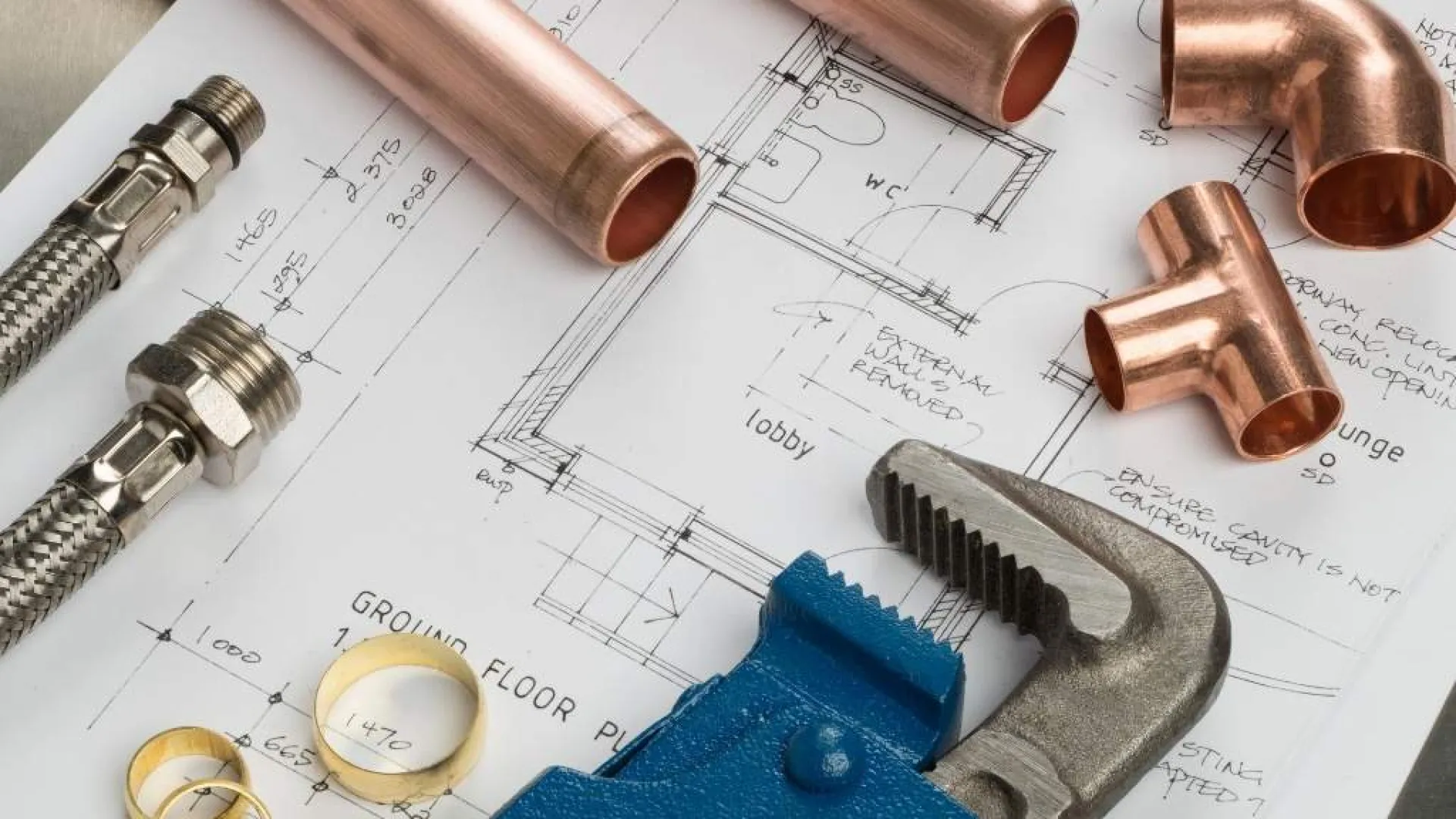 Copper pipes, fittings, adjustable wrench, and plumbing parts on building blueprint plans.