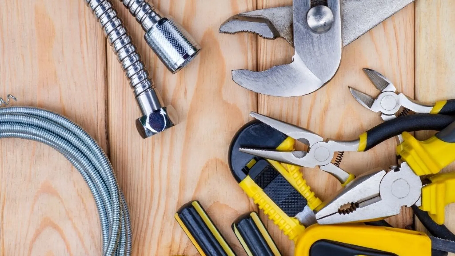 Plumbing tools and flexible metal hoses arranged on a wooden surface for repair work.