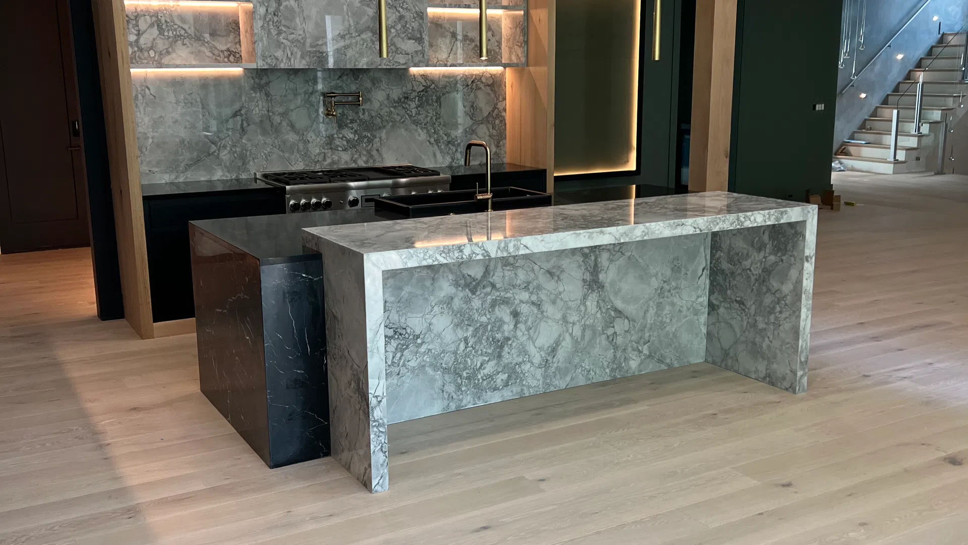 Modern kitchen with marble island and backsplash, wooden accents, pendant lights, and light hardwood flooring.