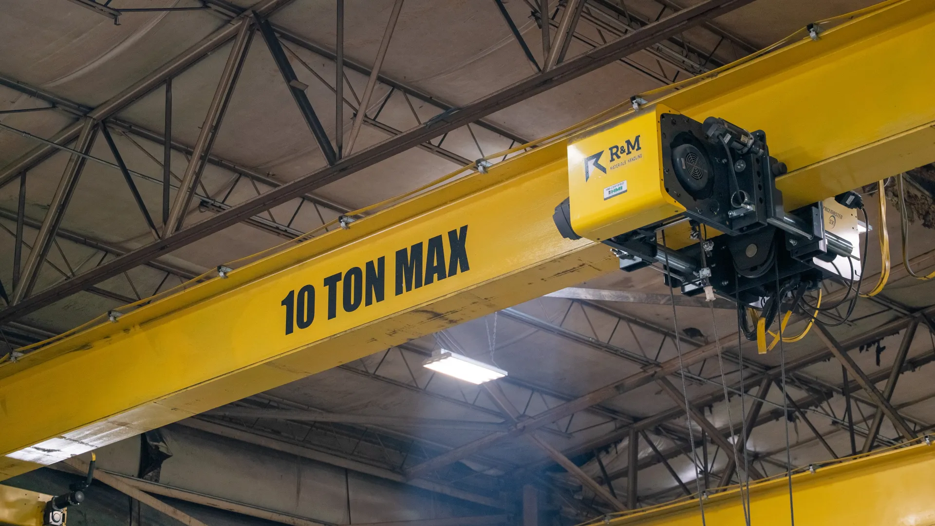 Yellow industrial overhead crane with 10 ton max capacity in a warehouse ceiling.