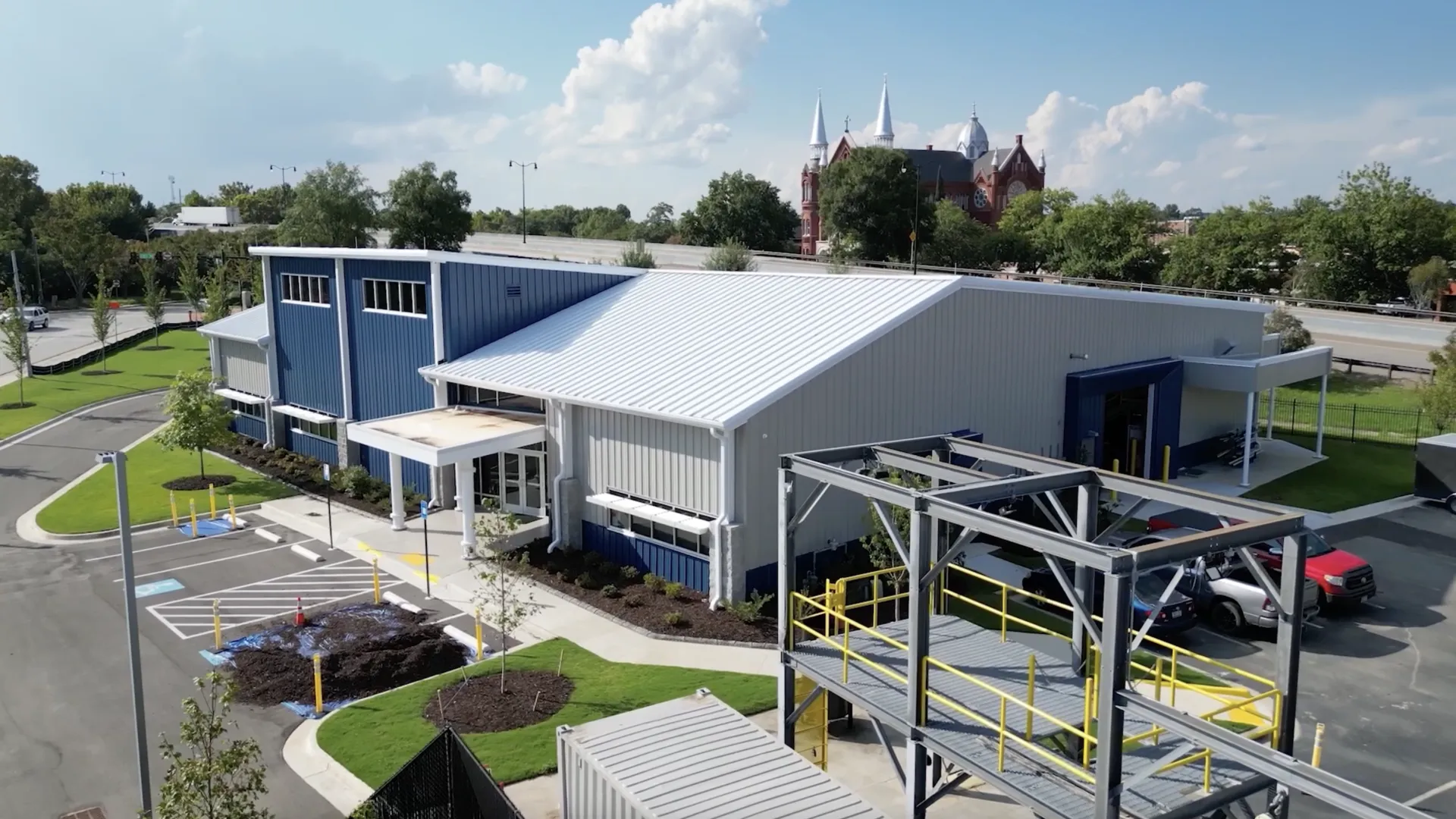 Aerial view of a modern commercial building with blue accents and surrounding landscaping under a clear sky.