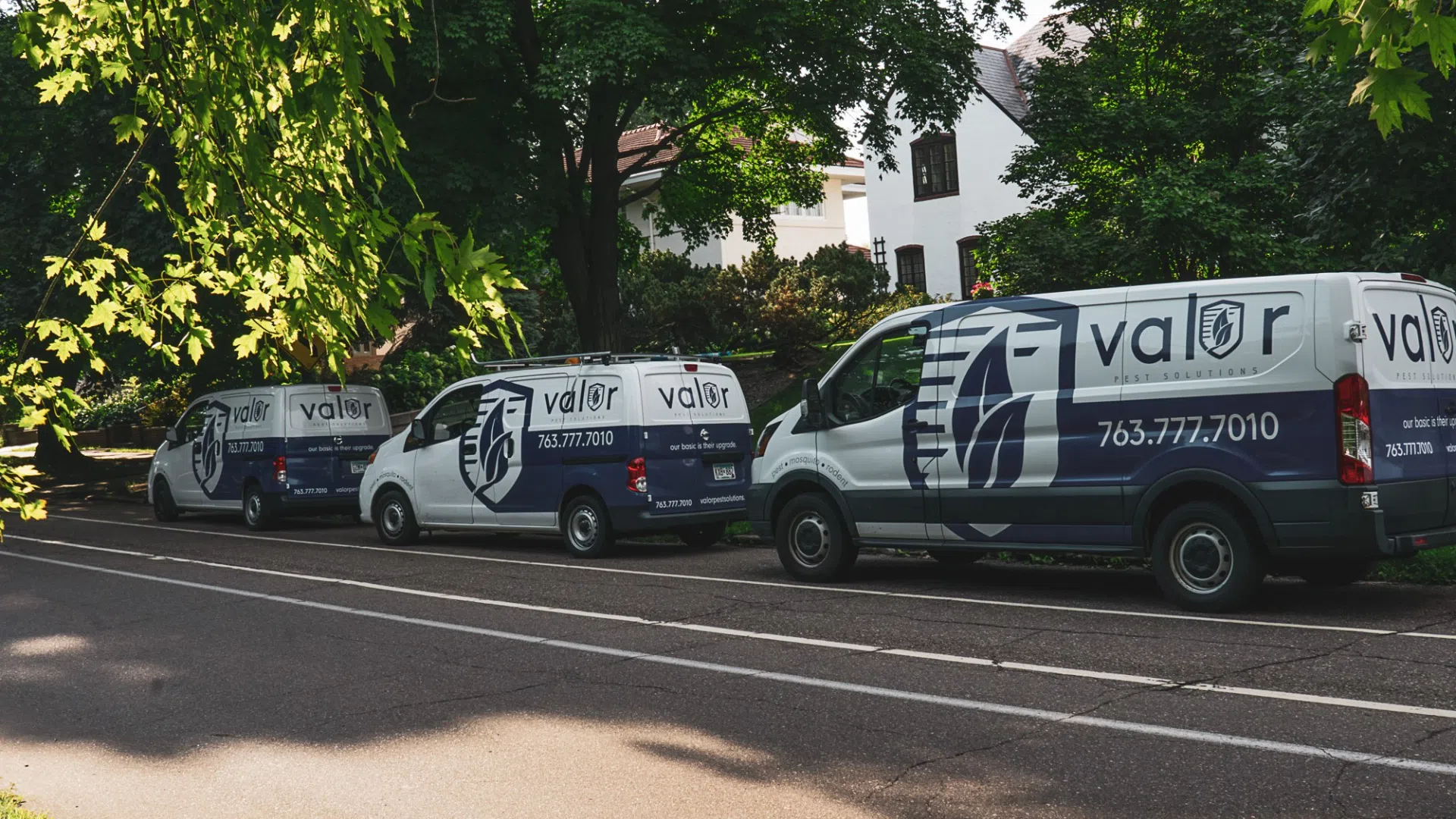 Three Valor Security vans parked in a row on a shaded residential street with trees and houses.